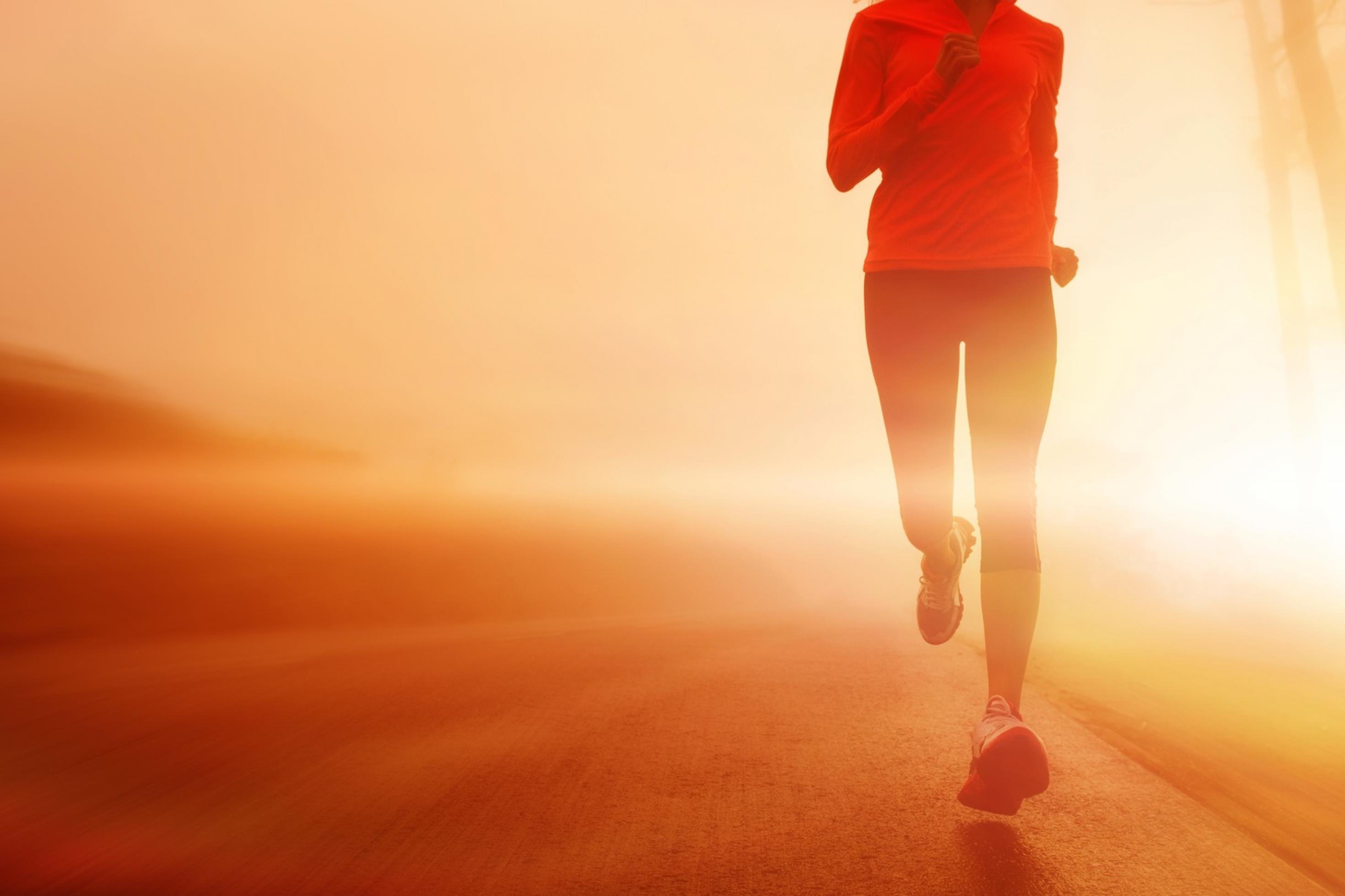 Eine Läuferin trainiert für den Marathonlauf. Ihr Gesicht ist nicht zu sehen. Hinter ihr geht die Sonne auf.