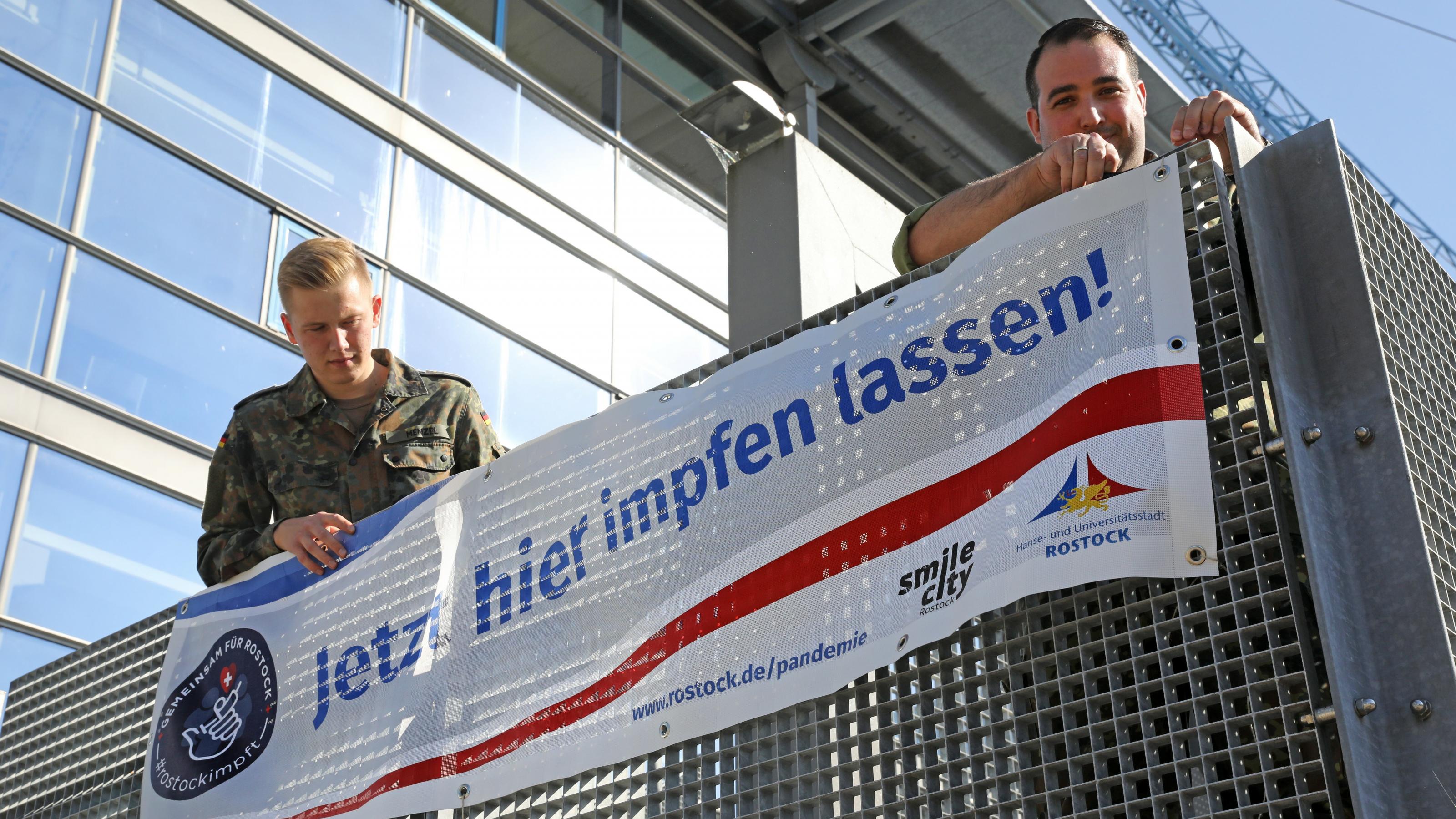 Impfaktion in Rostock: Helfer hängen ein Plakat für Corona-Impfung auf.