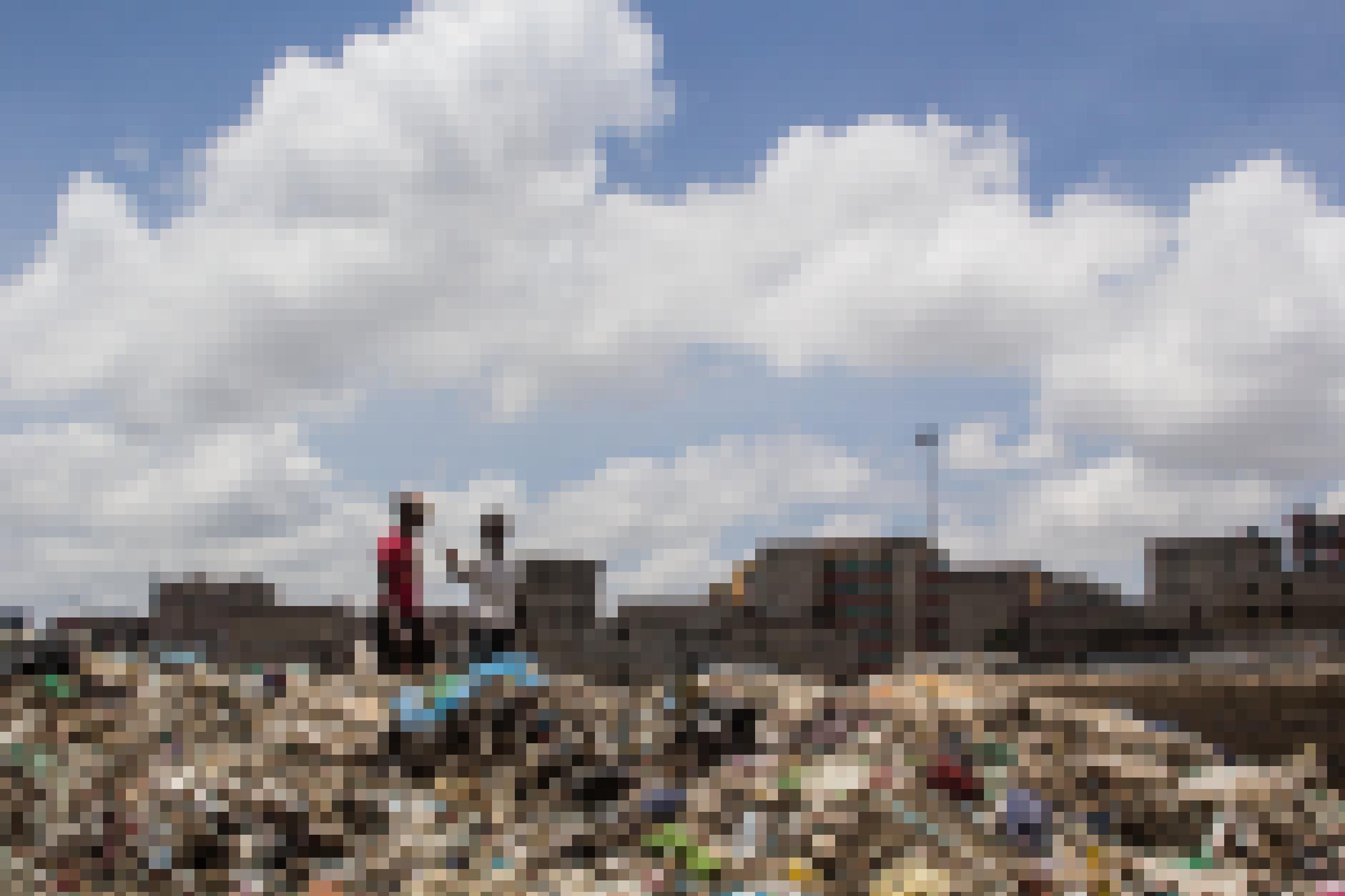 Am Rande der Hauptstraße von Mathare türmt sich Müll in einem hohen Berg, darauf sind zwei Menschen zu sehen, im Hintergrund mehrstöckige Häuser. Auf den Balkonen trocknet Wäsche.