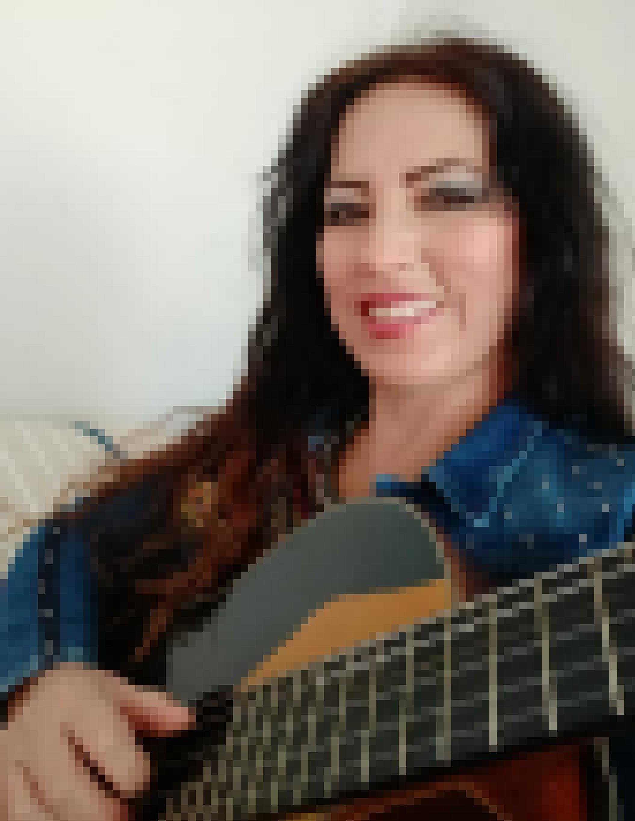 Hellhäutige Frau, Mitte 40, lange schwarze Haare, dunkle Augen, lächelt in die Kamera. In den Händen hält sie eine Gitarre.