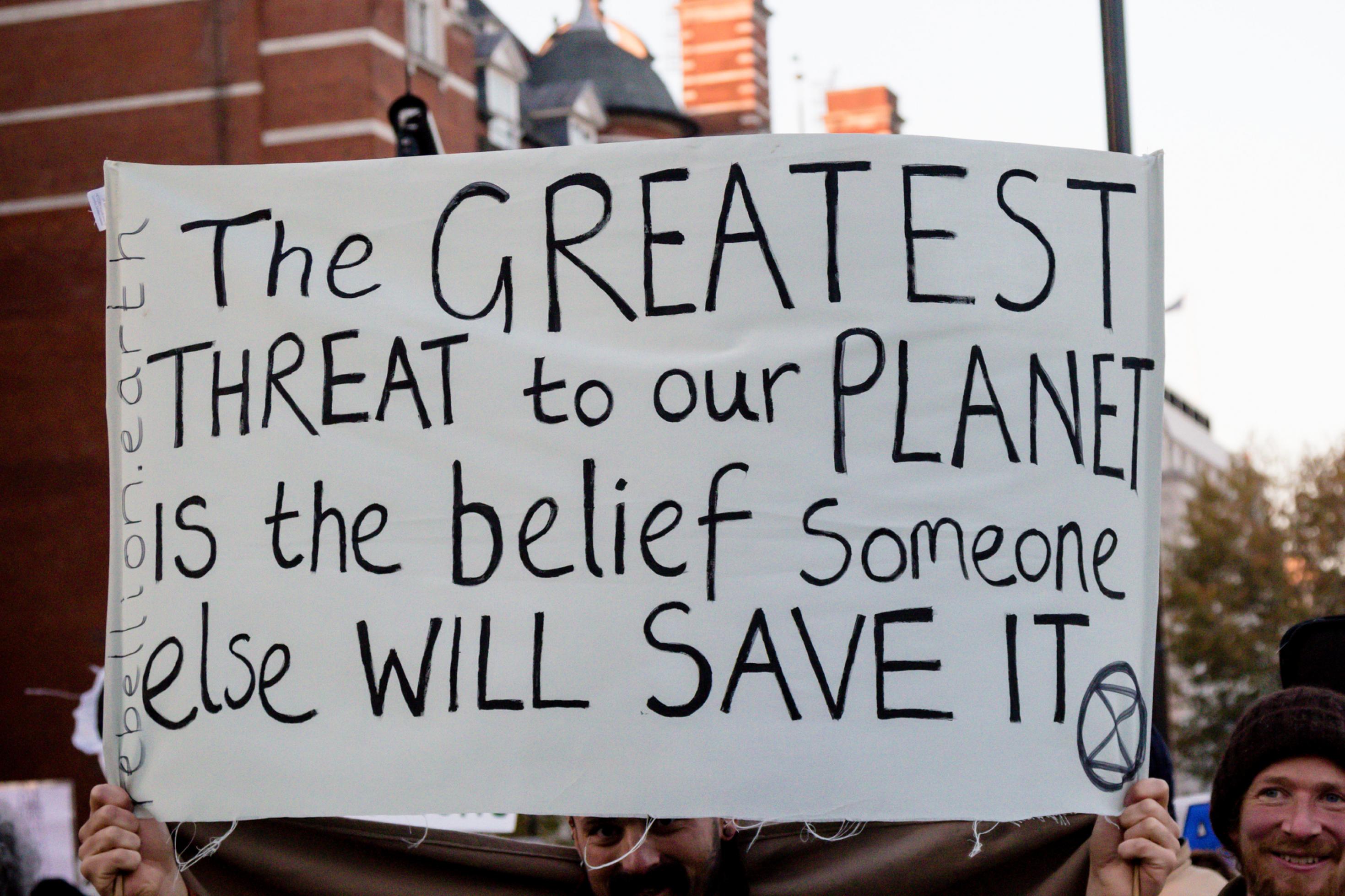 Mann hält bei einem Protest ein Transparent hoch, auf dem steht: „The greatest Threat to our Planet is the Belief someone else will save it“ (Die größte Gefahr für unseren Planten besteht in dem Glauben, jemand anderes wird ihn retten)