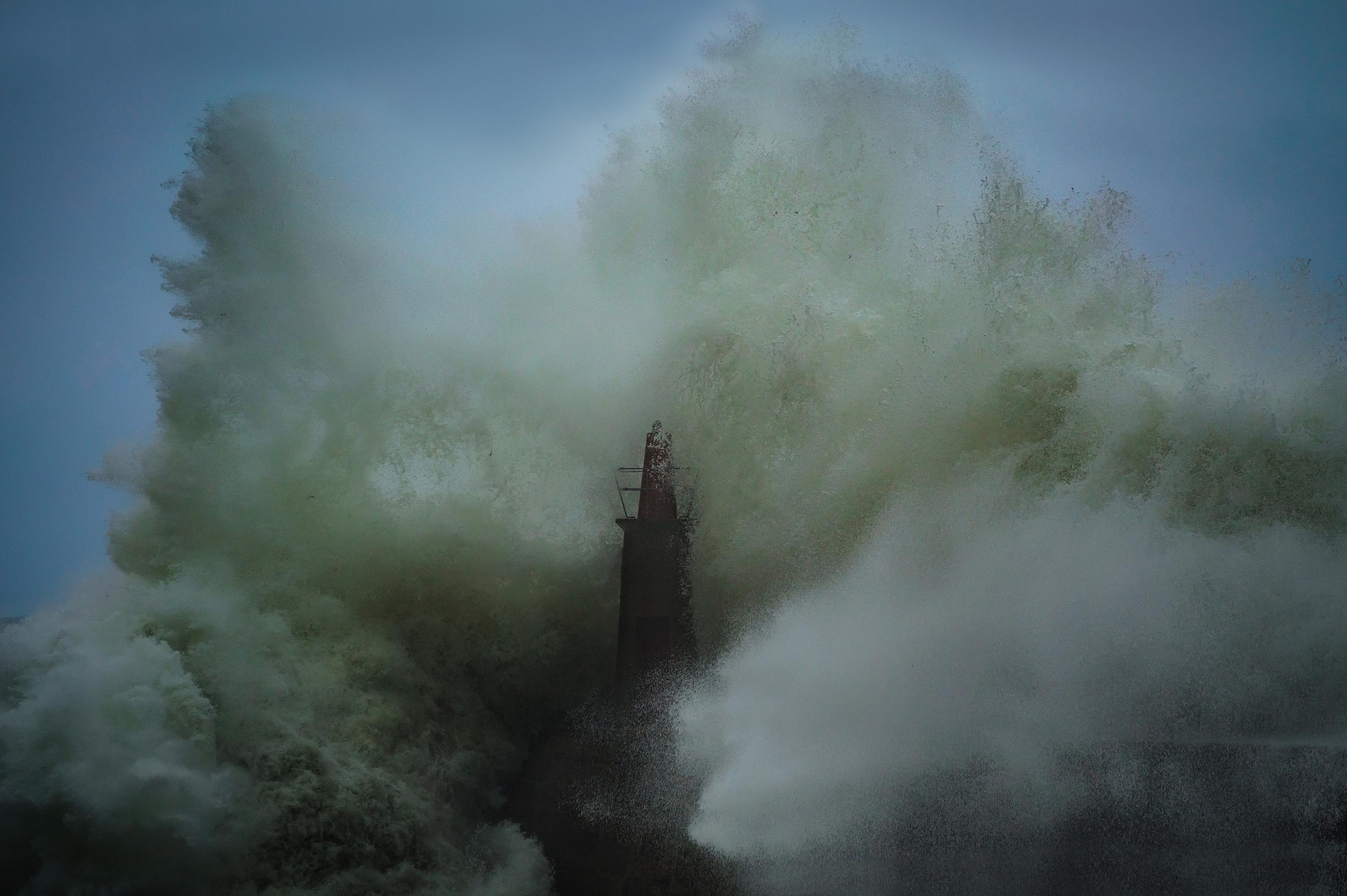 dunkelroter Leuchtturm wird von gischtschäumenden Riesenwellen überrollt