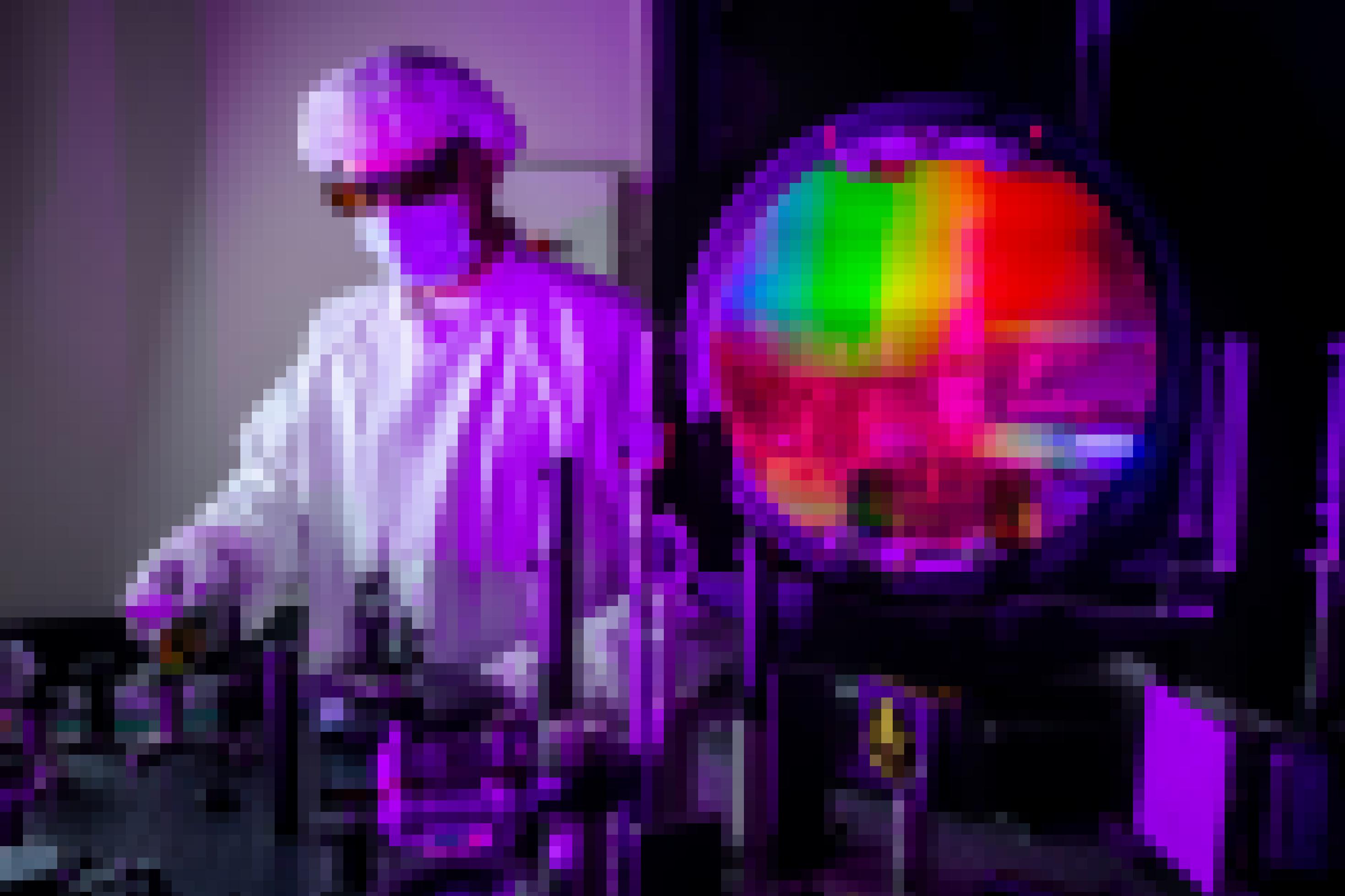 Ein Forscher in Ganzkörperschutzanzug steht vor einer Kammer, in der die Farben des Regenbogens zu sehen sind.