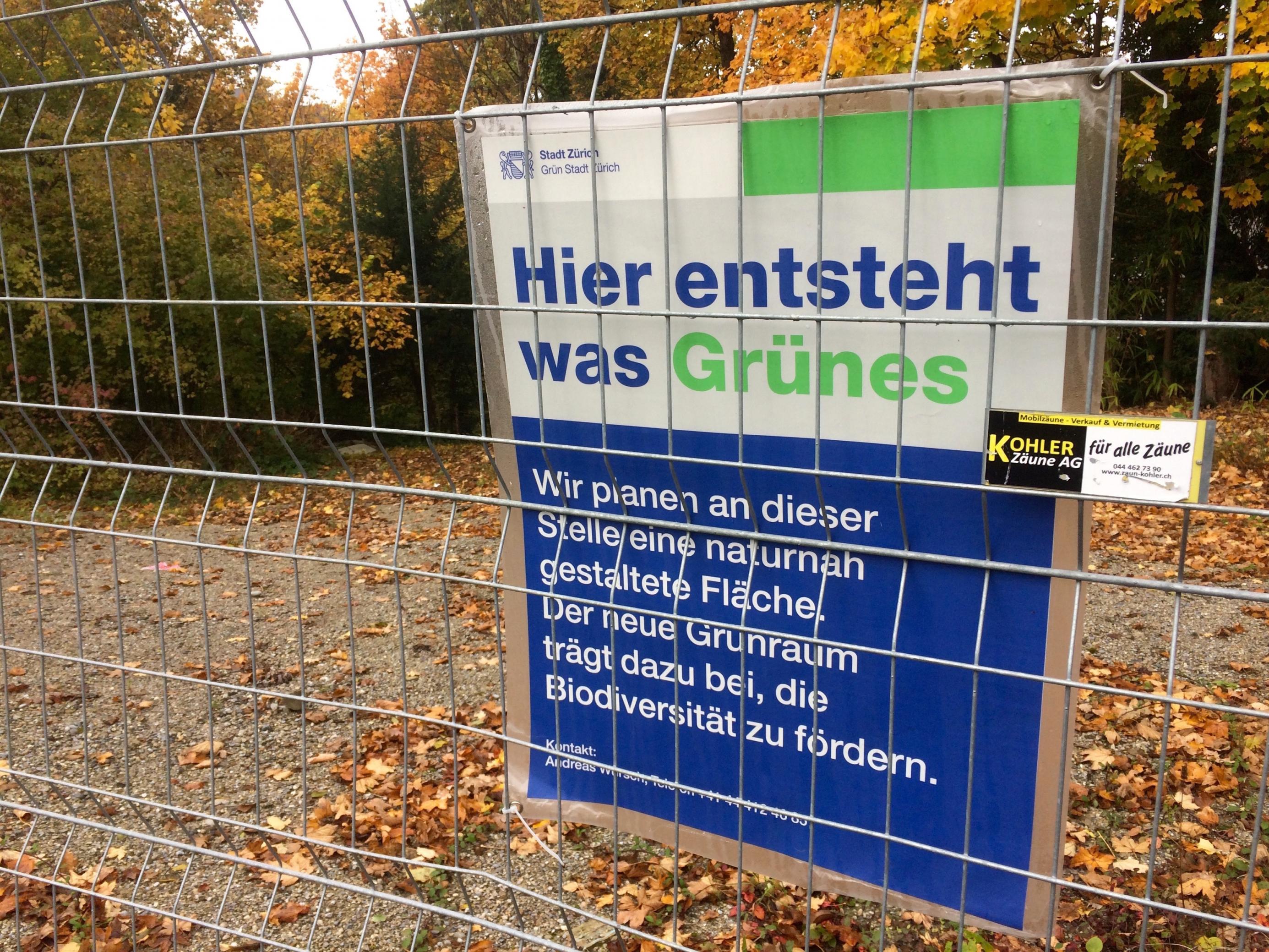 An einem Zaun in Zürich hängt ein Plakat der Stadtverwaltung, auf dem die Wiederherstellung der Biodiversität am Rande einer Strasse angekündigt wird.