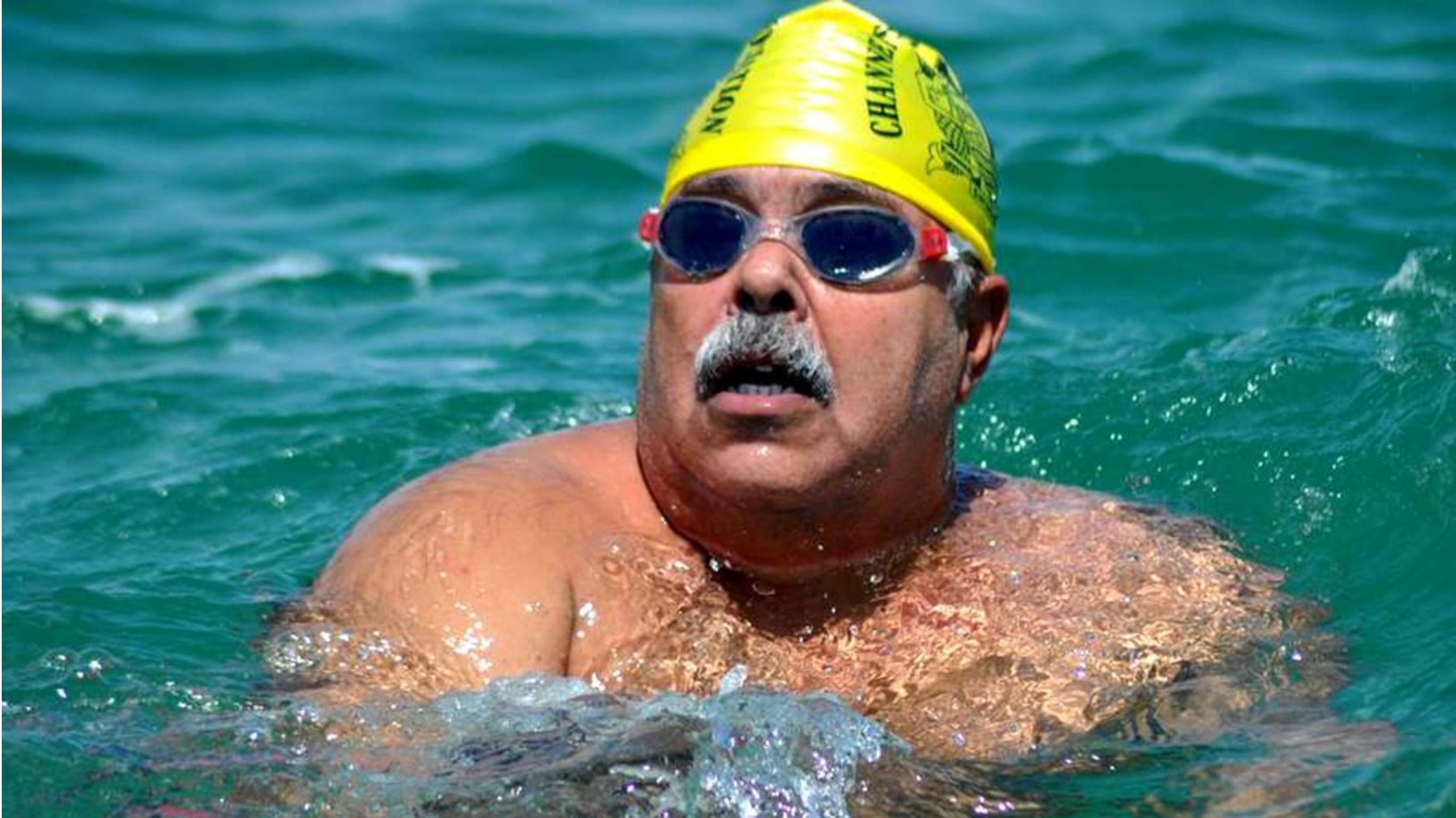 Ein Mann mit Schwimmbrille und -mütze schaut aus dem Wasser