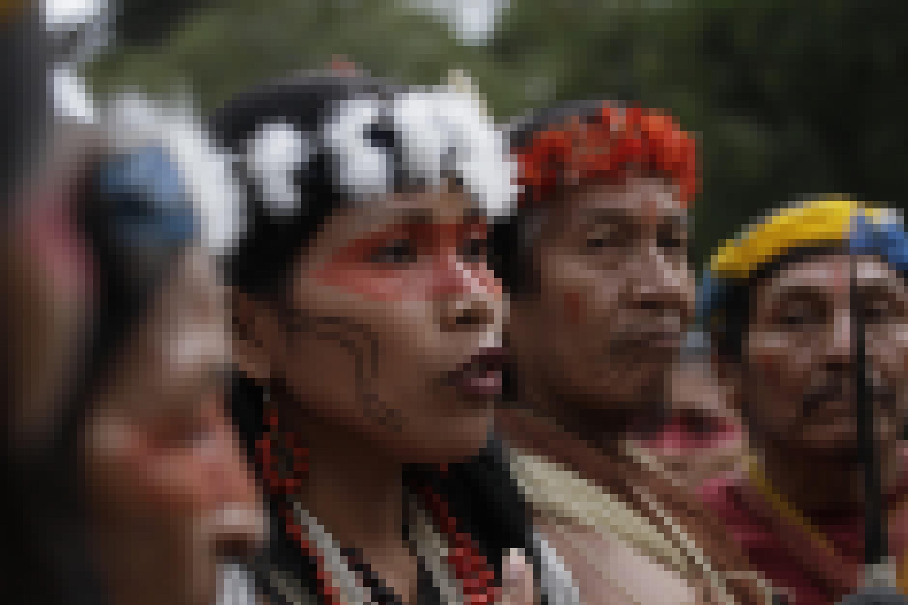 Die Aktivistin Nemonete Nenquimo steht neben weiteren Aktivisten der Waorani-Gemeinschaft. Ihre Augenpartie ist rot bemalt. Auf dem Kopf trägt sie eine Federkrone.