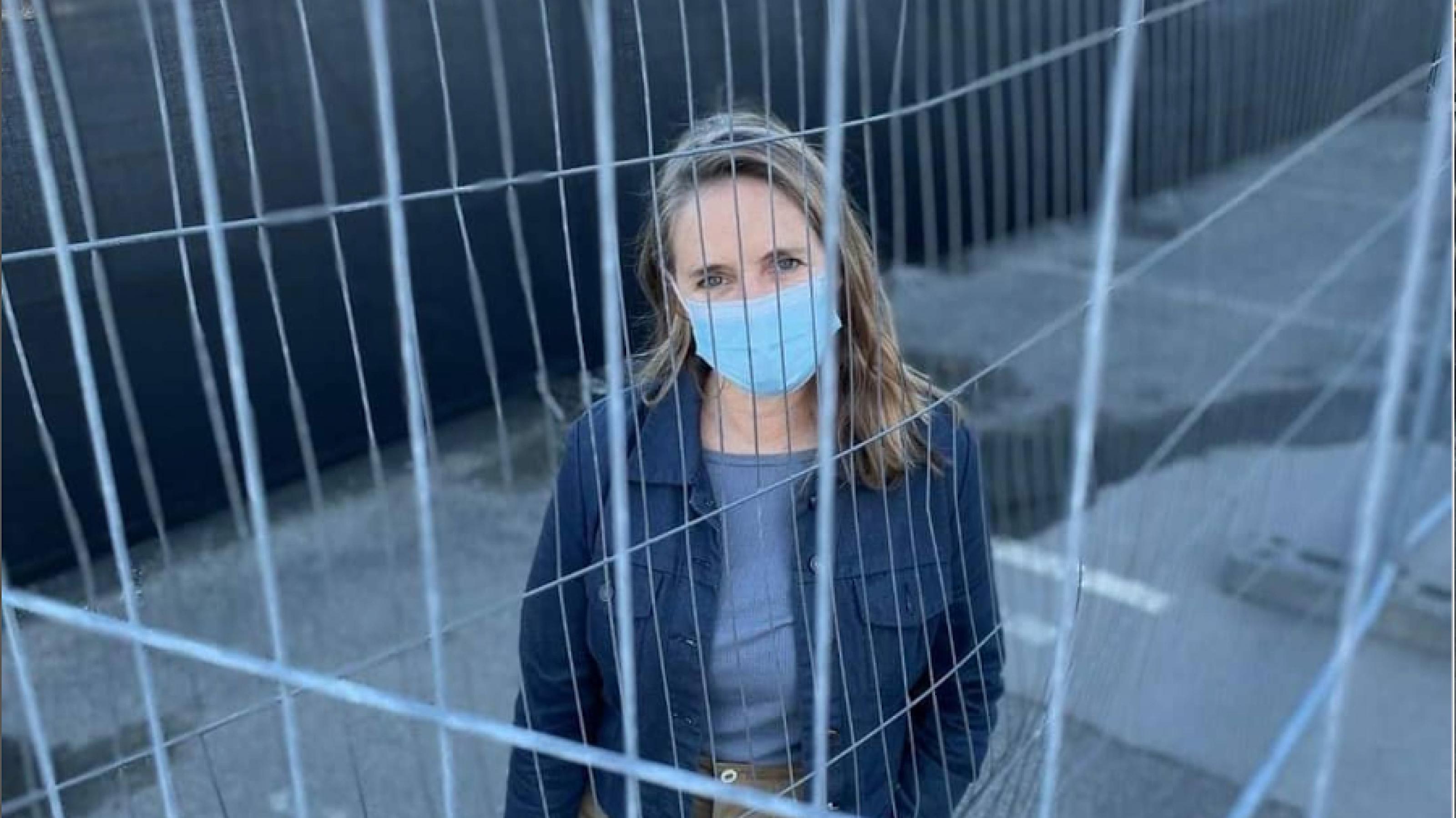 Neuseeland-Korrespondentin schaut mit ihrer Gesichtsmaske durch den Zaun des Quarantänehotels