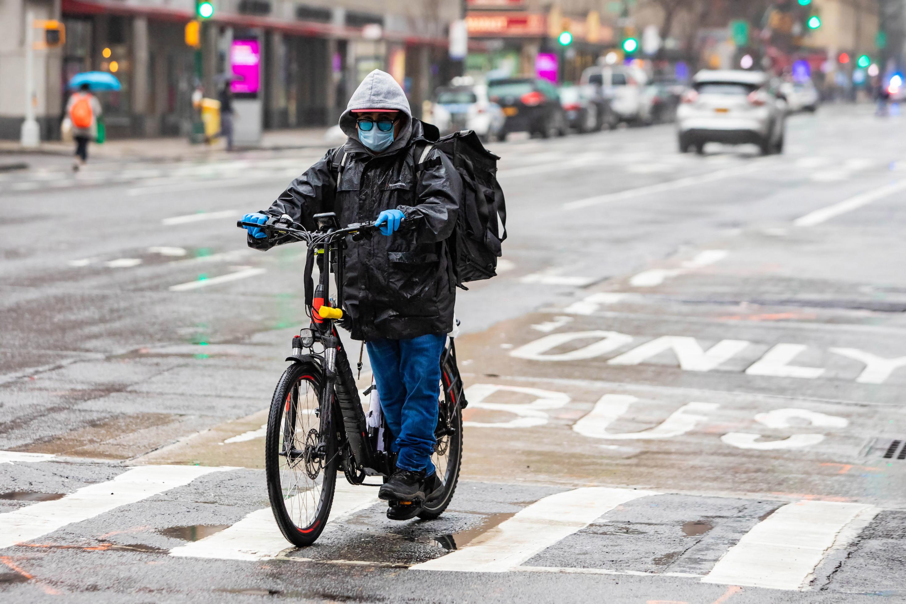 Ein Mann schiebt ein Fahrrad. Er trägt einen Mundschutz und Regenkleidung. Das Bild mutet an wie aus einem Science Fiction.