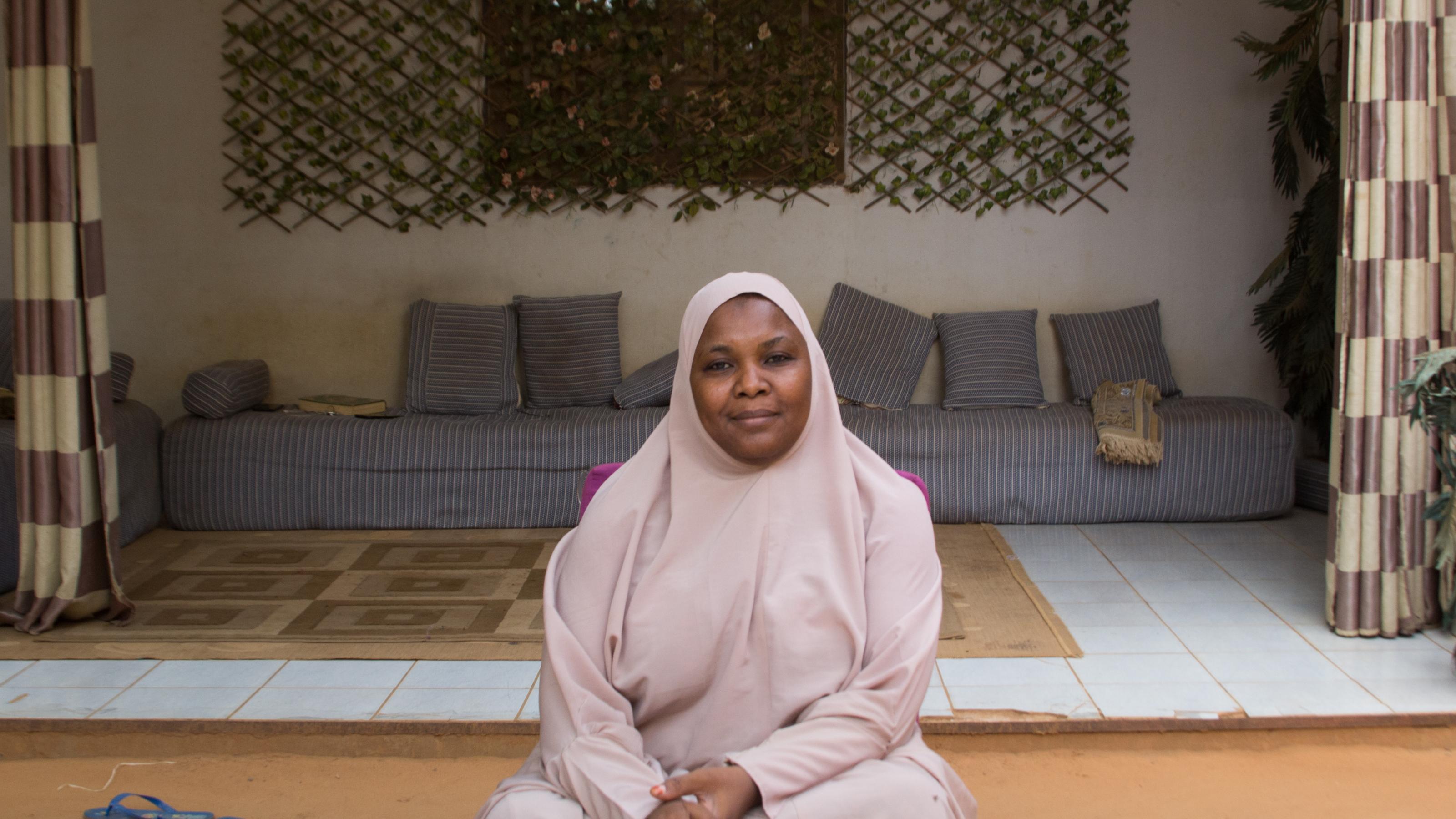 Malama Sakına trägt einen rosafarbenen Ganzkörperschleier. Im Hintergrund die Sitzgelegenheiten auf der Veranda ihres Hauses.