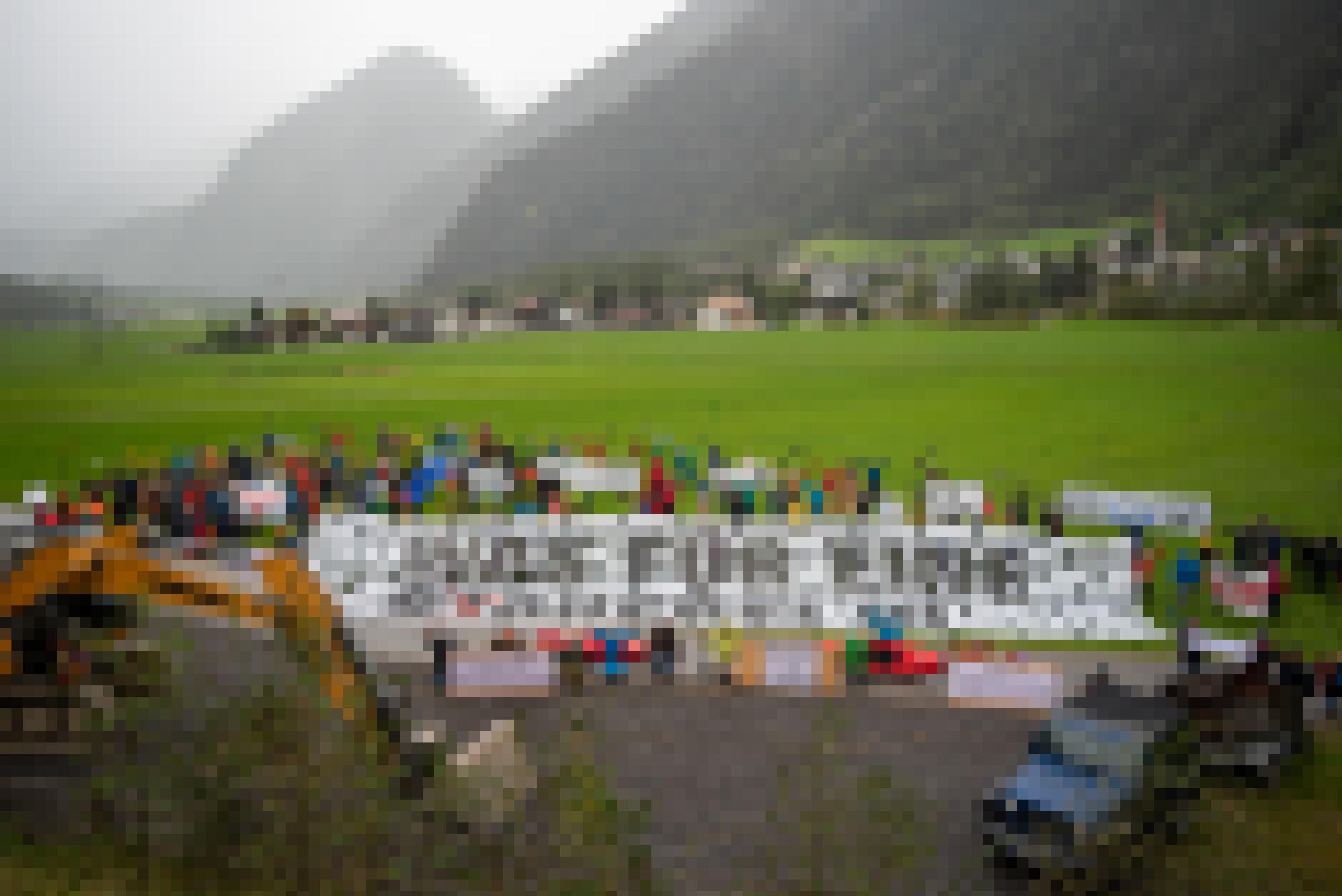 Menschen stehen auf einer Wiese am Rande eines Dorfes mit einem großen Banner mit der Aufschrift: Was für eine Stauerei.