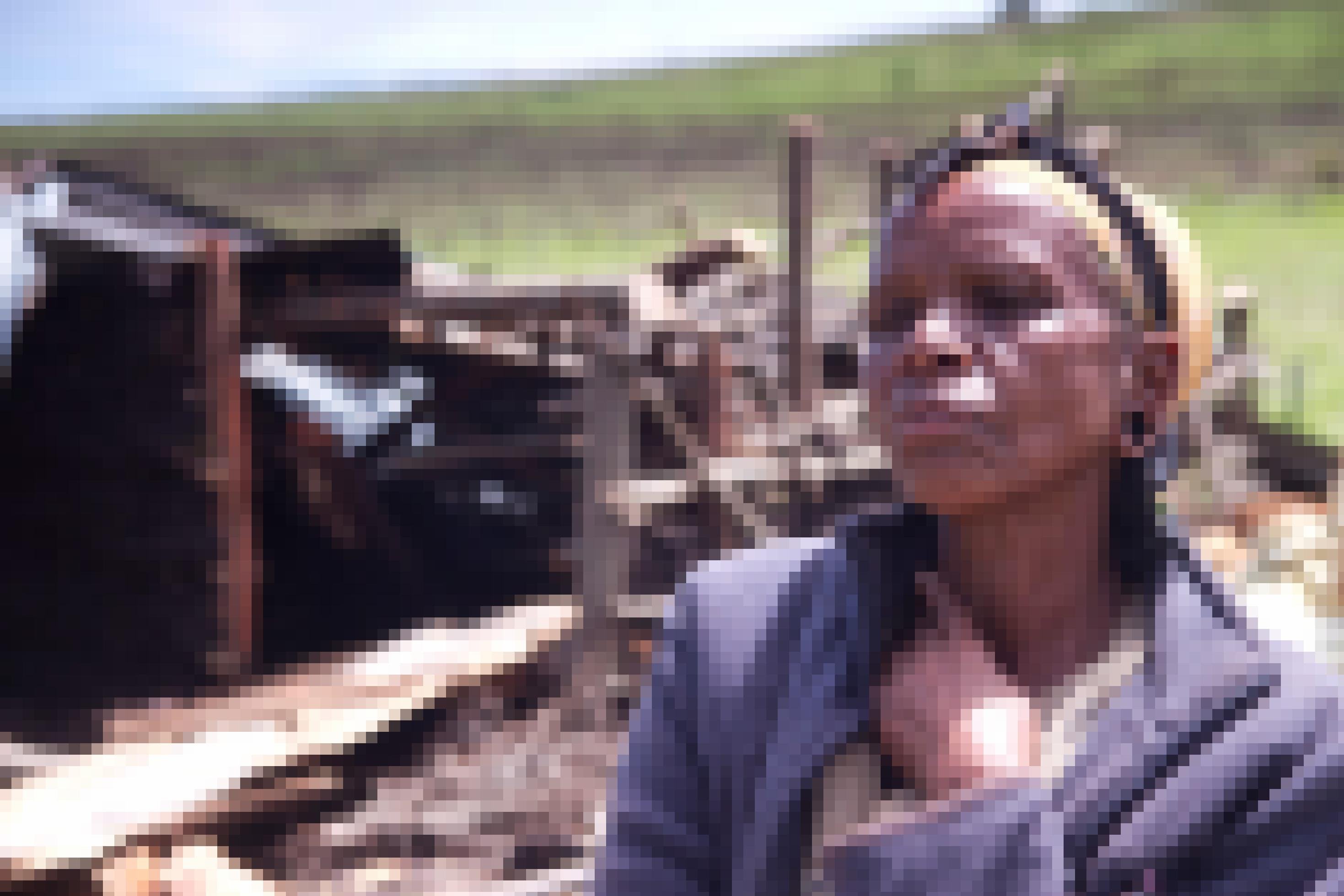 Im Vordergrund ist eine Ogiek-Frau zu sehen mit traurigem Blick, im Hintergrund die Überreste ihres abgebrannten und zerstörten Hauses in Kenia.