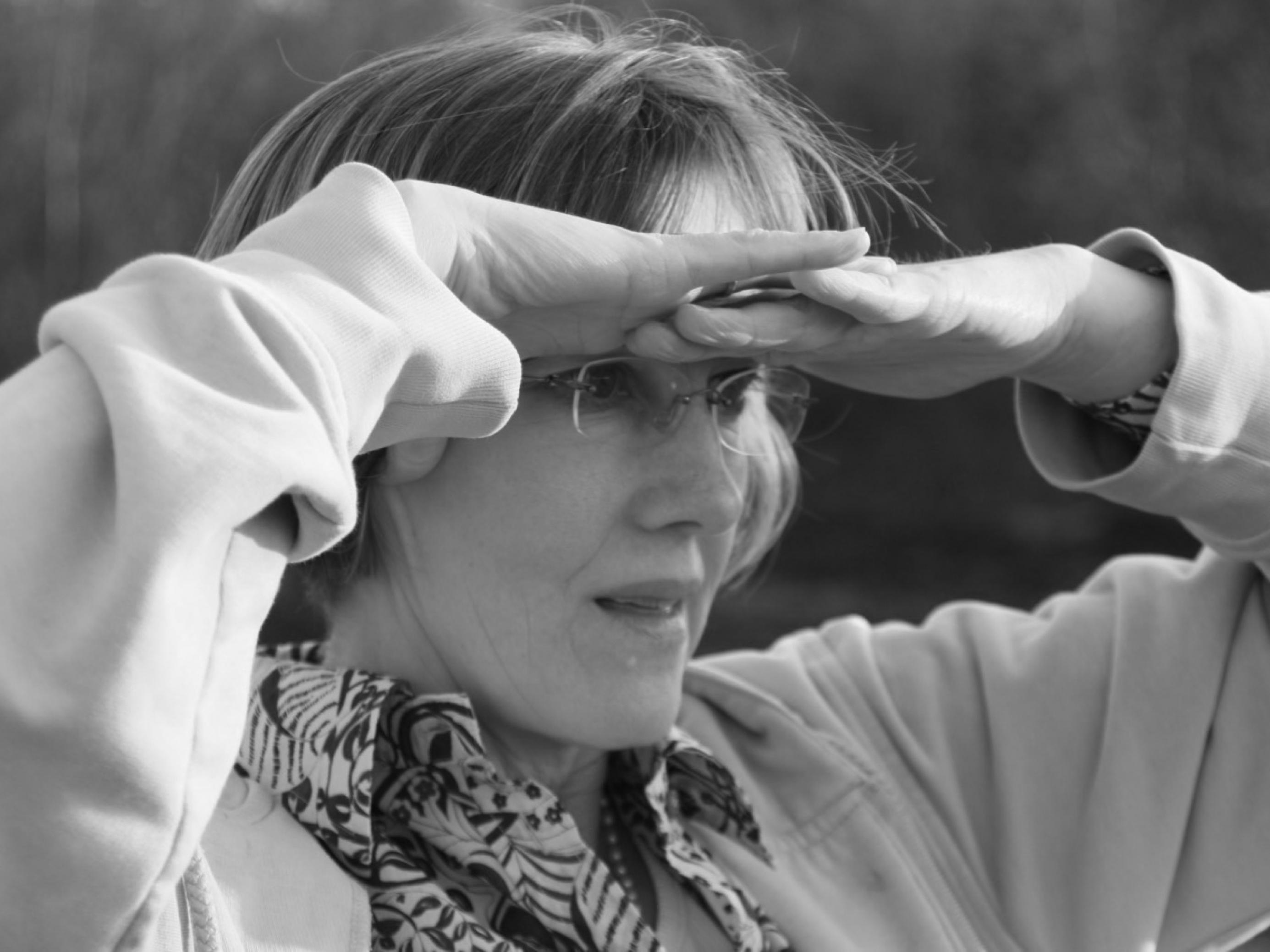Zu sehen ist die Autorin Johanna Romberg. Auf dem Foto schirmt sie mit beiden Händen ihre Augen ab und blickt in die Ferne.