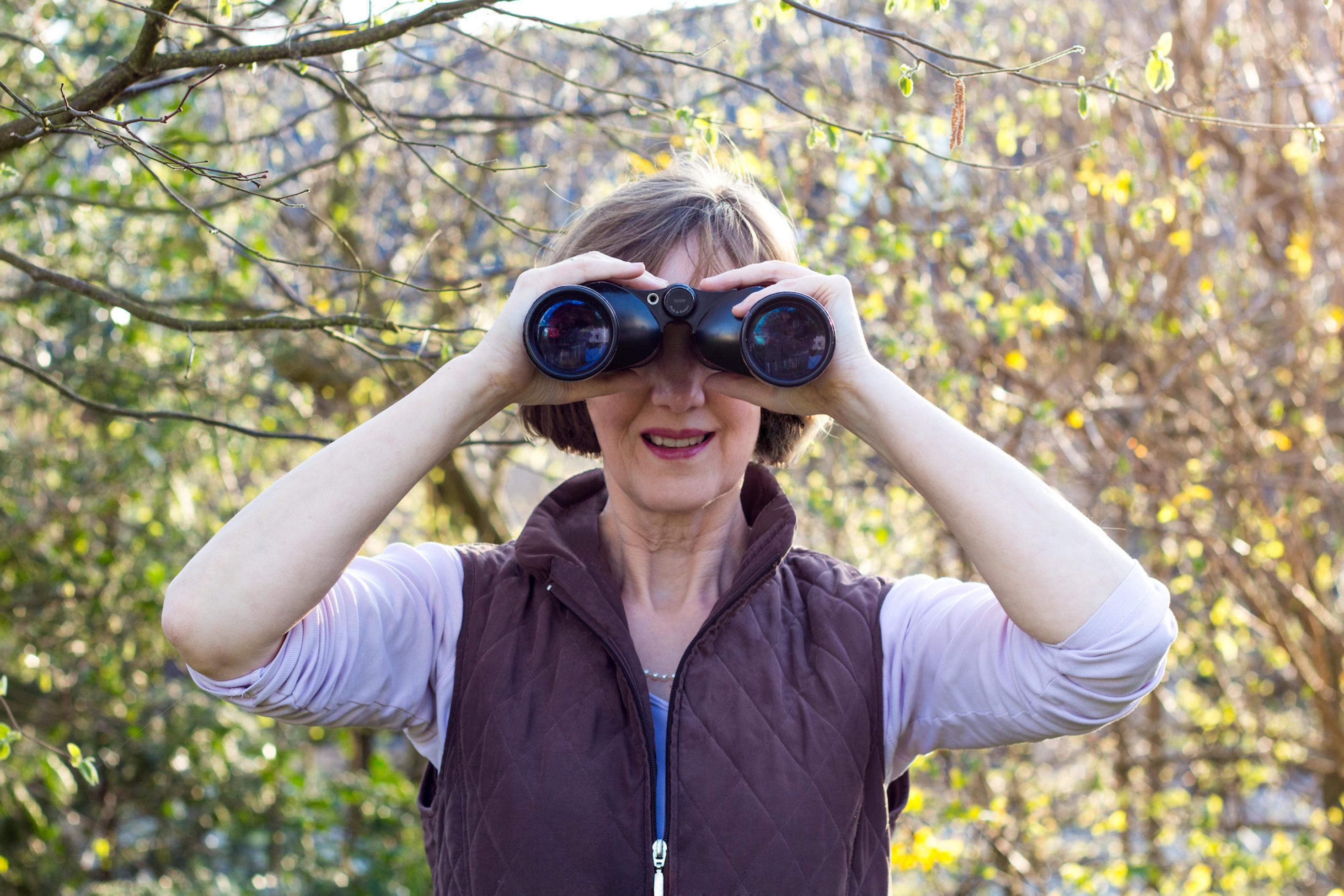 Die Umweltjournalistin Johanna Romberg ist Vogelbeobachterin, das Bild zeigt sie, während sie durch ein Fernglas blickt.