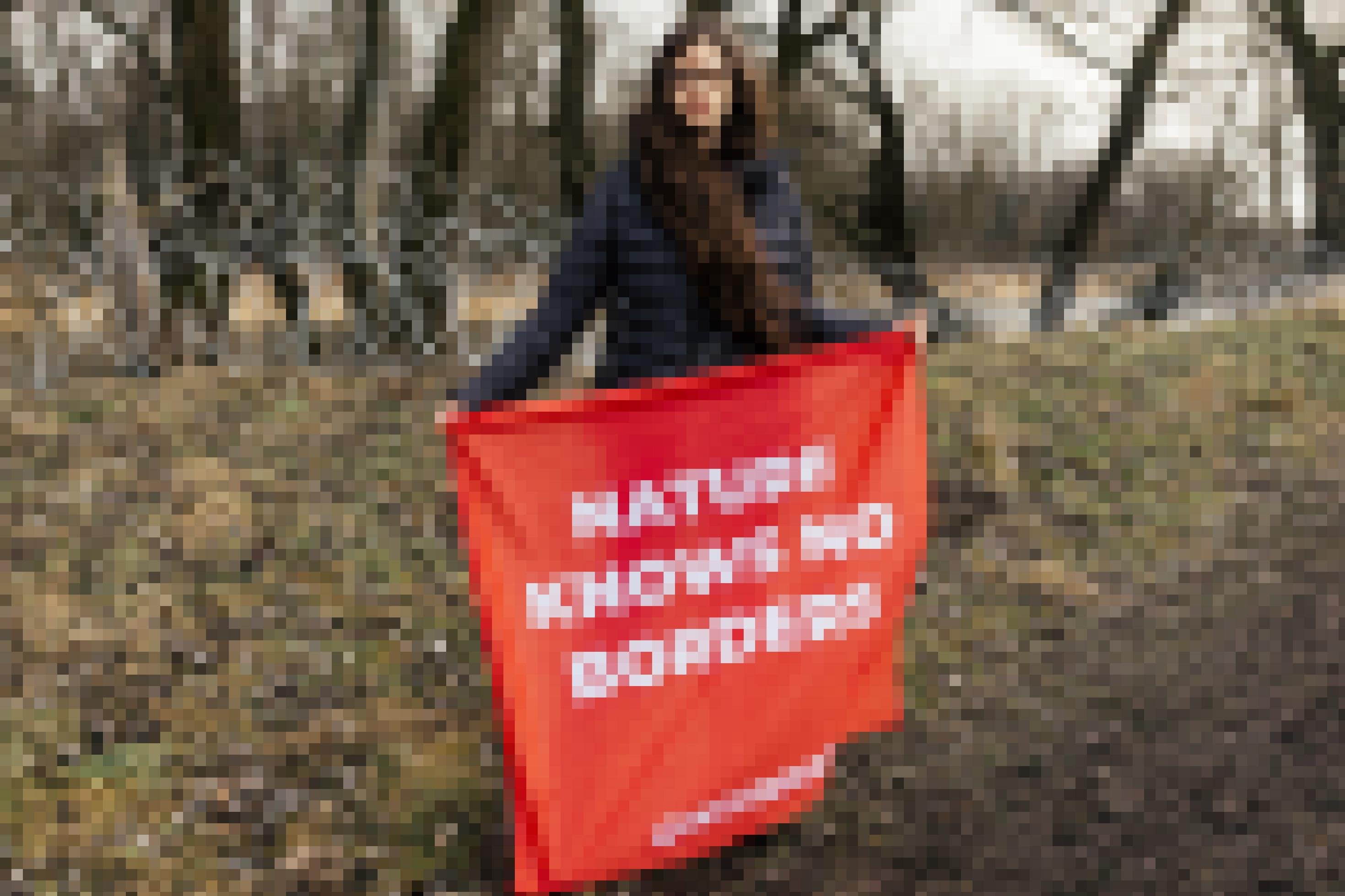Eine Greenpeace-Aktivistin protestiert am Grenzfluss Bug gegen die Einzäunung. Mit einem Plakat „Natur kennt keine Grenzen“ steht sie vor Stacheldrahtrollen am Flussufer.