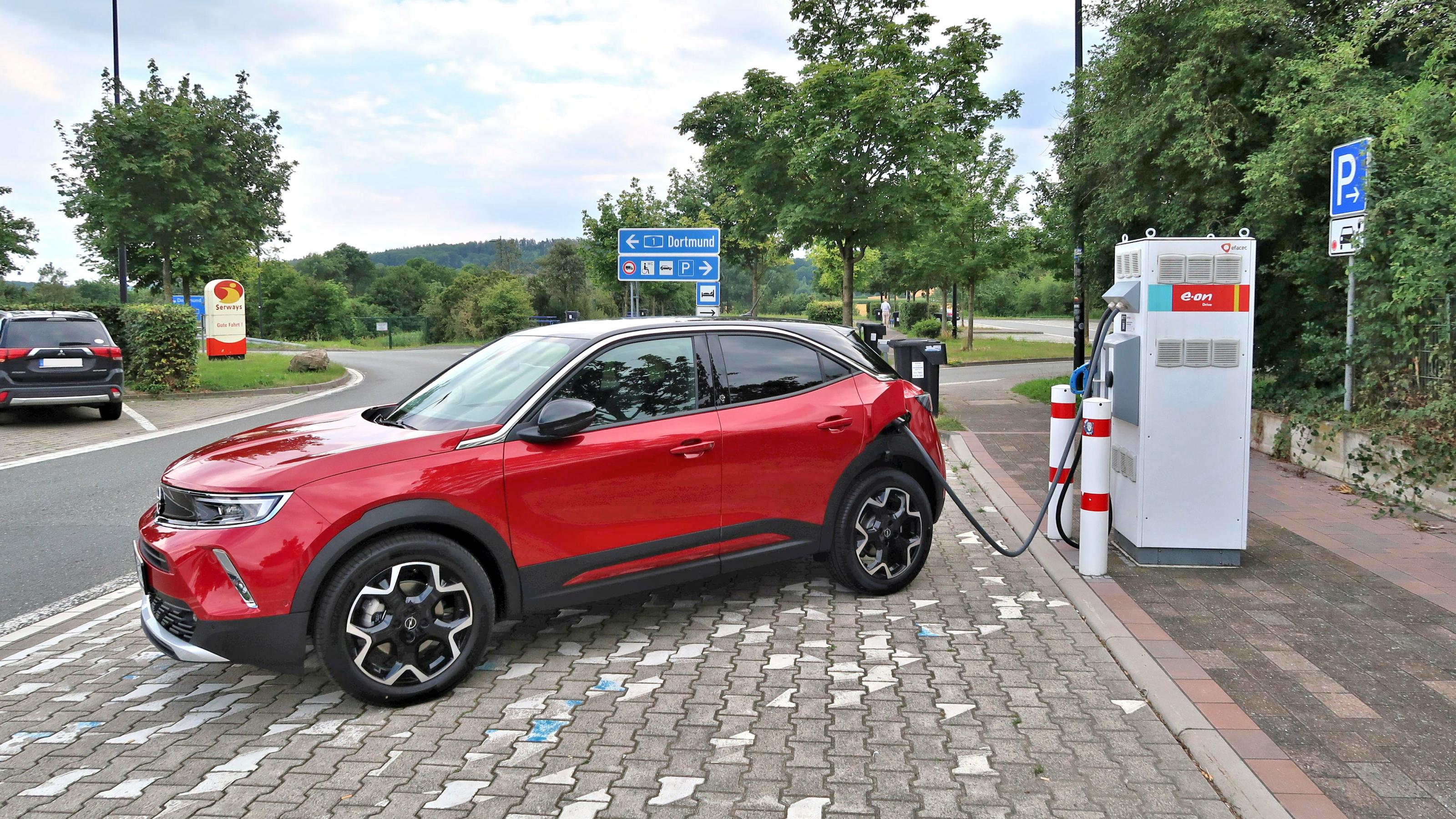 Ein roter Opel Mokka-E lädt auf einer Autobahnraststätte Strom.