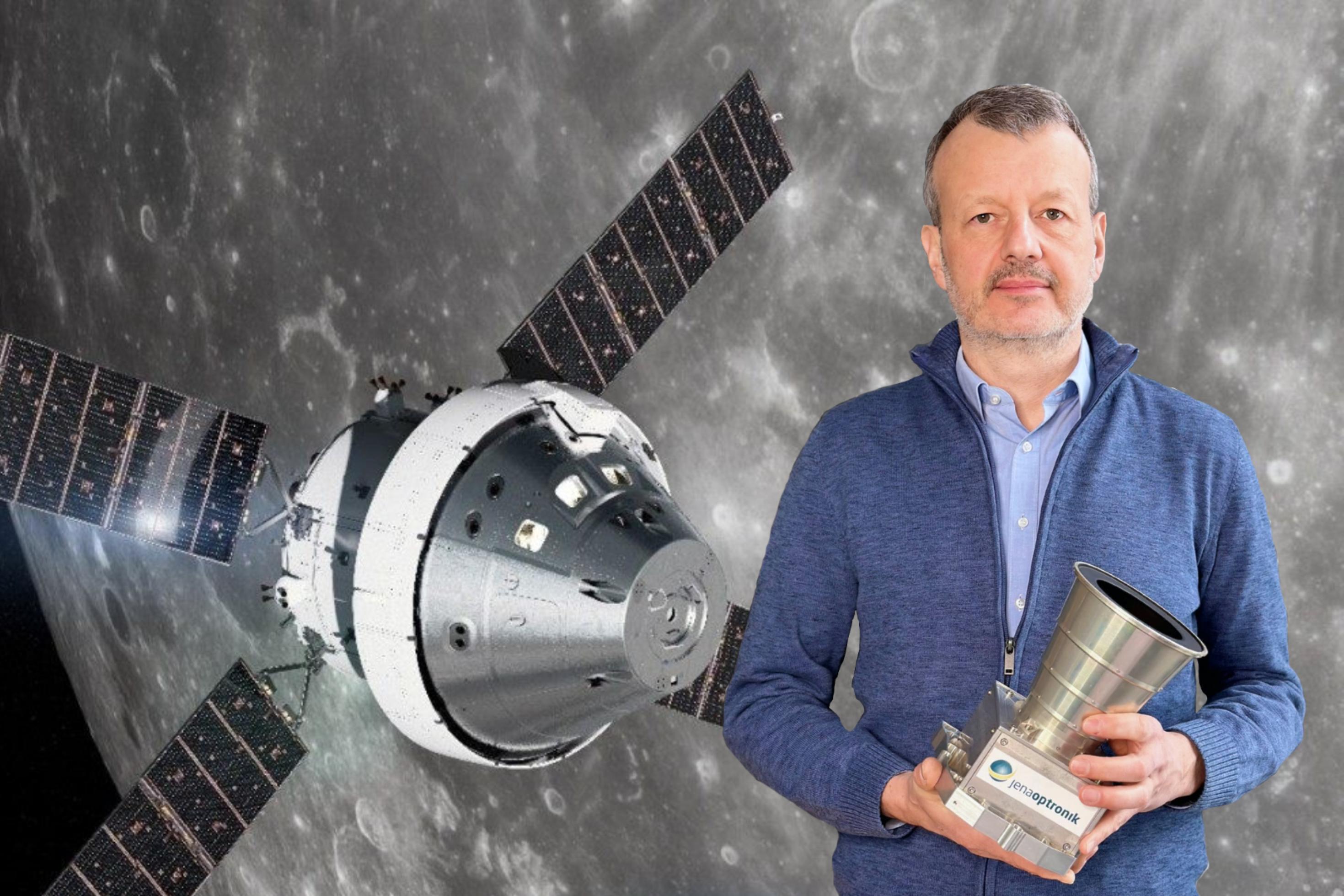 Andreas Deter von der Jena-Optronik hält einen Sternsensor in der Hand (rechts im Vordergrund). Dieser sieht wie eine metallische Kamera mit langem Objektiv aus. Im Hintergrund ist eine Illustration vom Orion-Raumschiff am Mond zu sehen. Der Sternsensor wird das Raumschiff zum Mond navigieren.