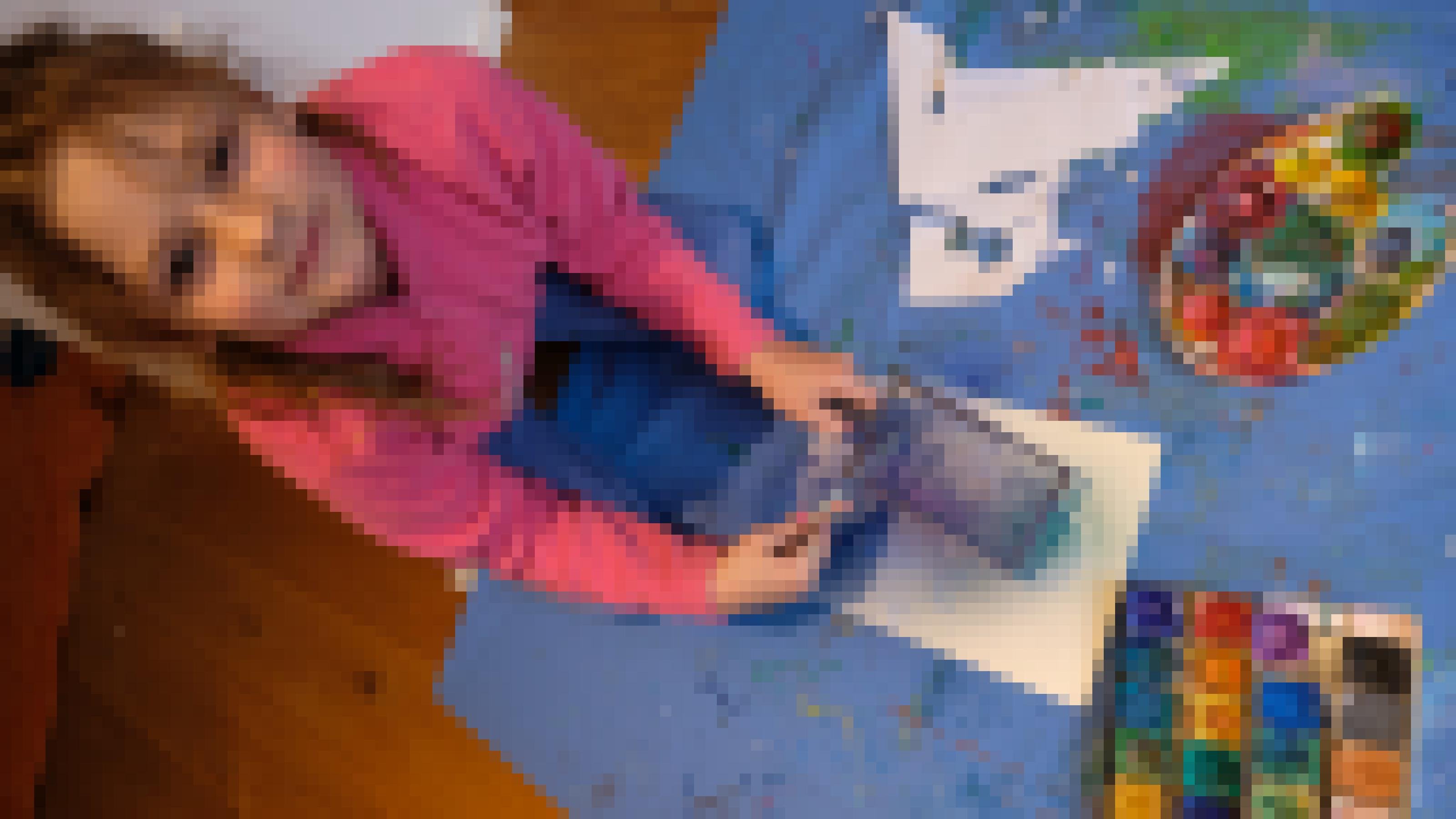 Auf einer blauen Wachstischdecke hockt die achtjährige Orla über ihrem Blatt Papier. Vor ihr liegen der Wasserfarbkasten und eine bunte Palette zum Farbenmischen. Sie guckt in die Kamera. Links hält sie ein Sieb, rechts eine Zahnbürste mit Farbe. Auf dem Papier sind schon ein paar Spritzer verteilt.