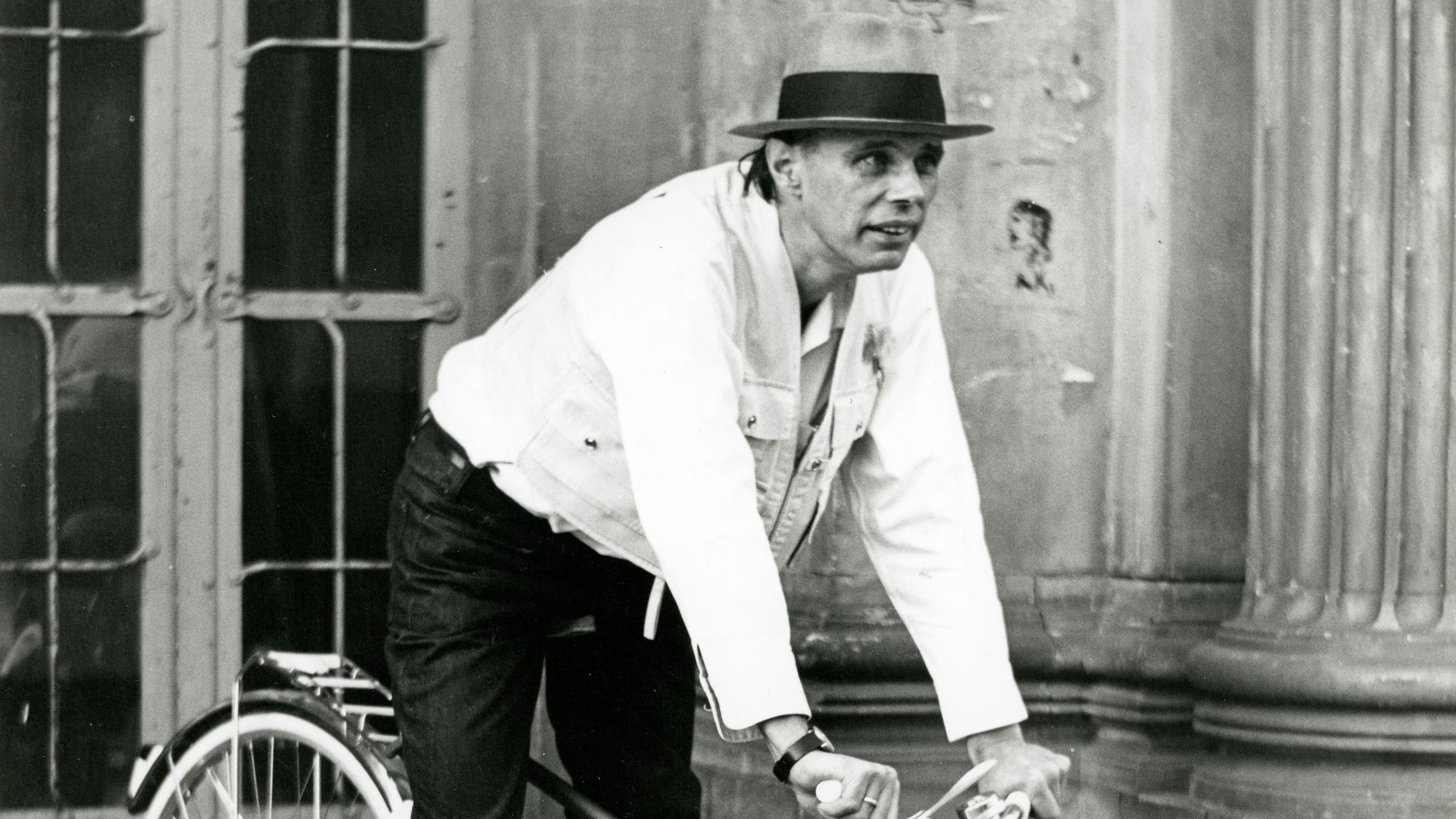 Beuys fährt ii Mountainbike-Stil, gekleidet mit weißem Hemd und dunkler Hose, drei flache Steinstufen hinunter.