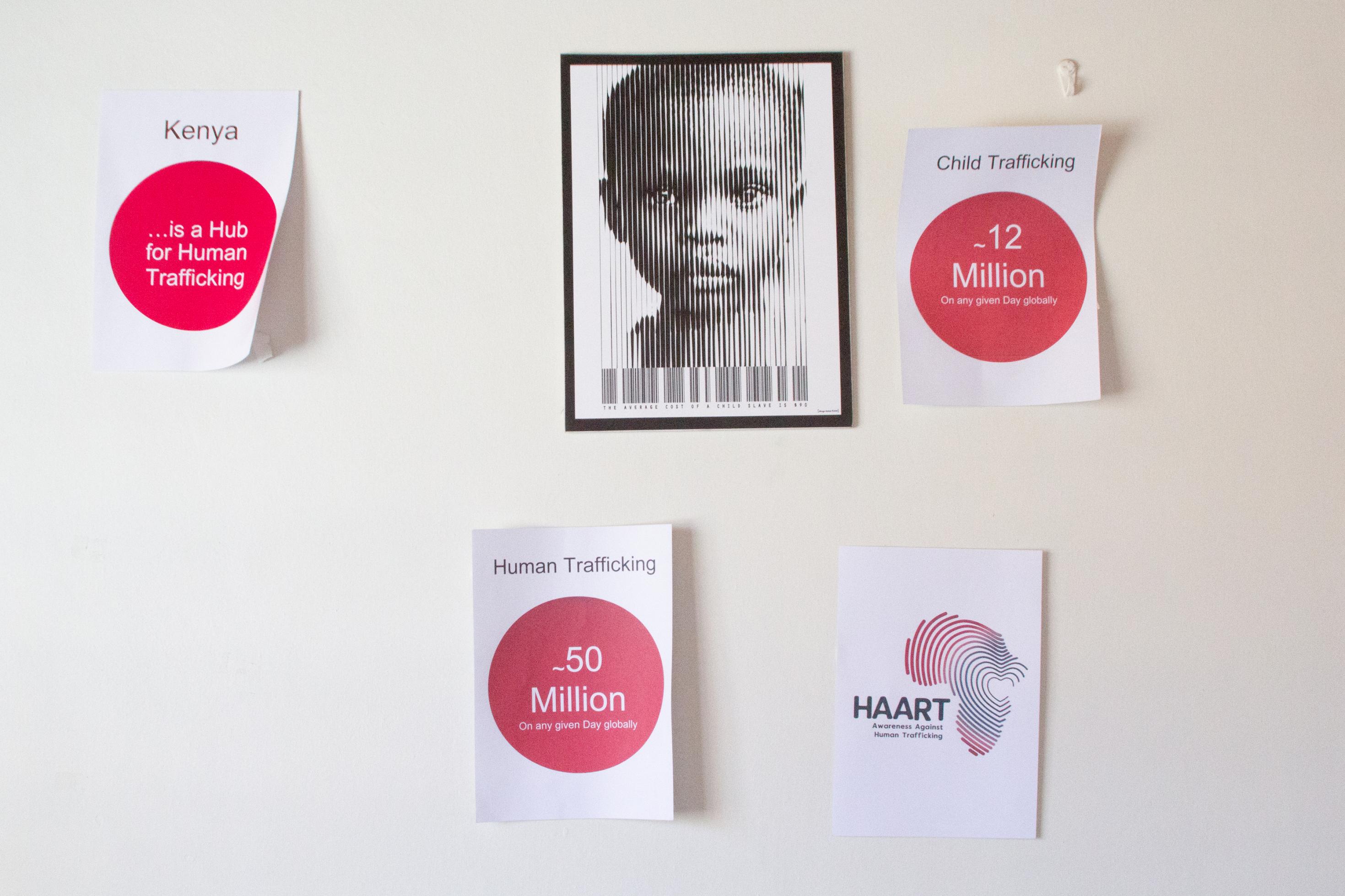 Eine Wand mit DINA4-Blättern, auf denen einige Statistiken zum Menschenhandel und Sklavenarbeit stehen. Ein anderes Blatt trägt das Foto eines Kindes, verfremdet zu einem Barcode.