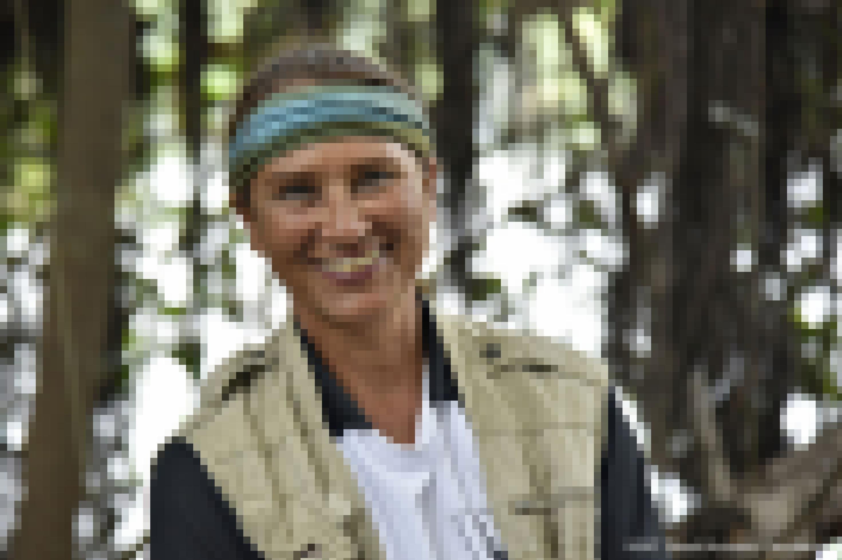 Freundlich lächelnde Frau mit grün-blauem Stirnband vor einem verschwommenen Regenwald