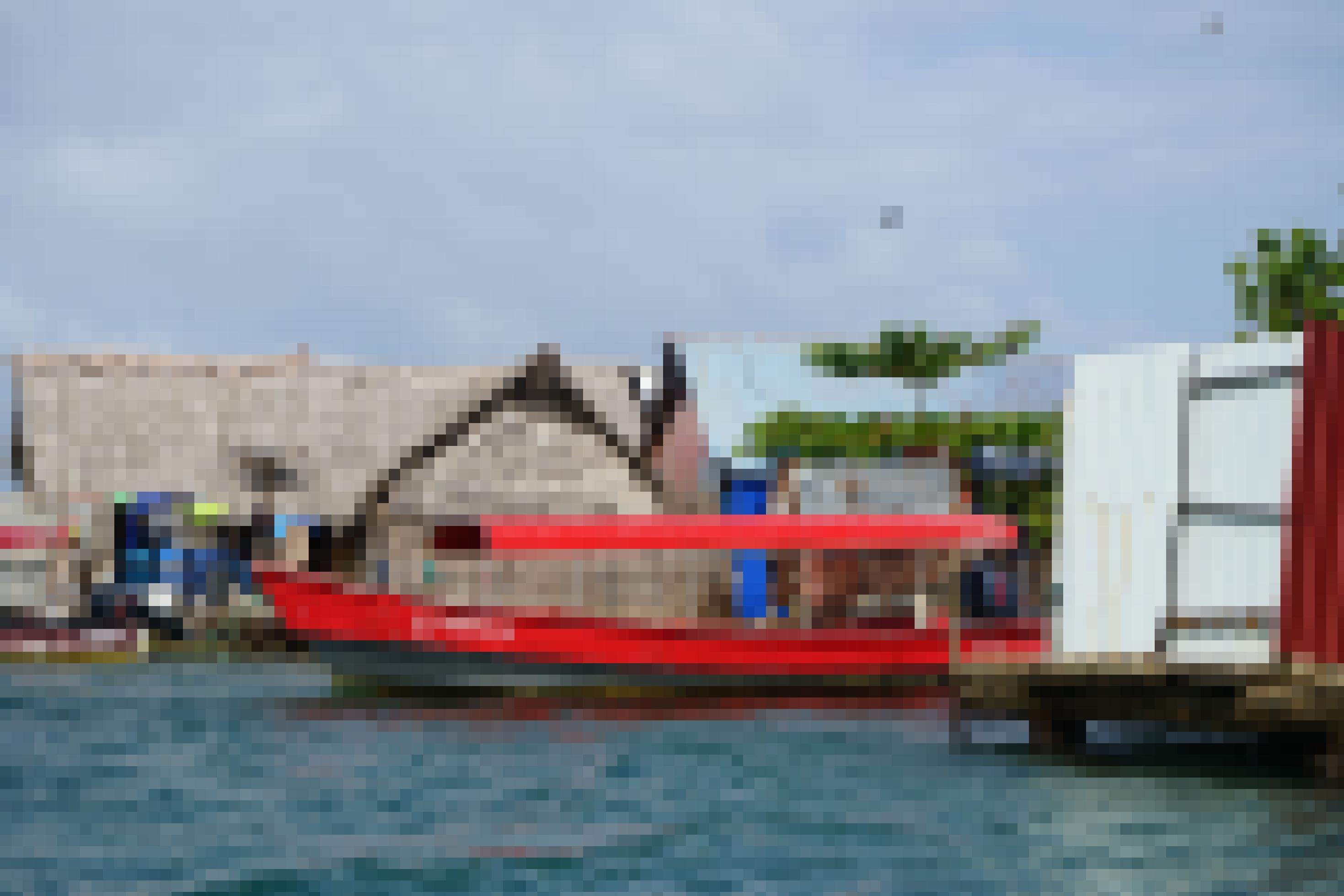 Ein rotes Boot dümpelt vor einer Kulisse von Holzhäusern im Meer.