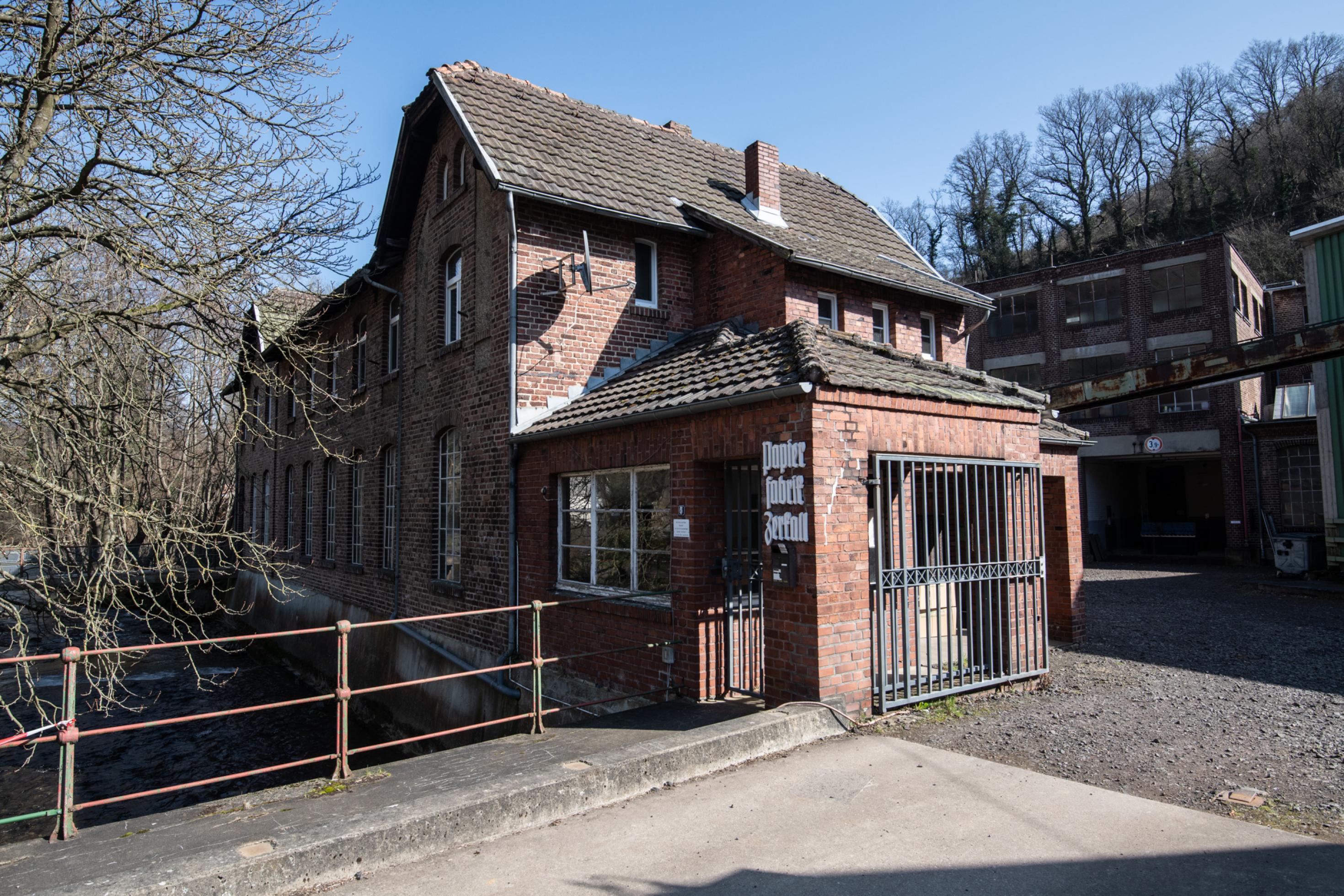 Einfahrt mit Backsteingebäude, an dessen Front in alter Schrift „Papierfabrik Zerkall“ steht.