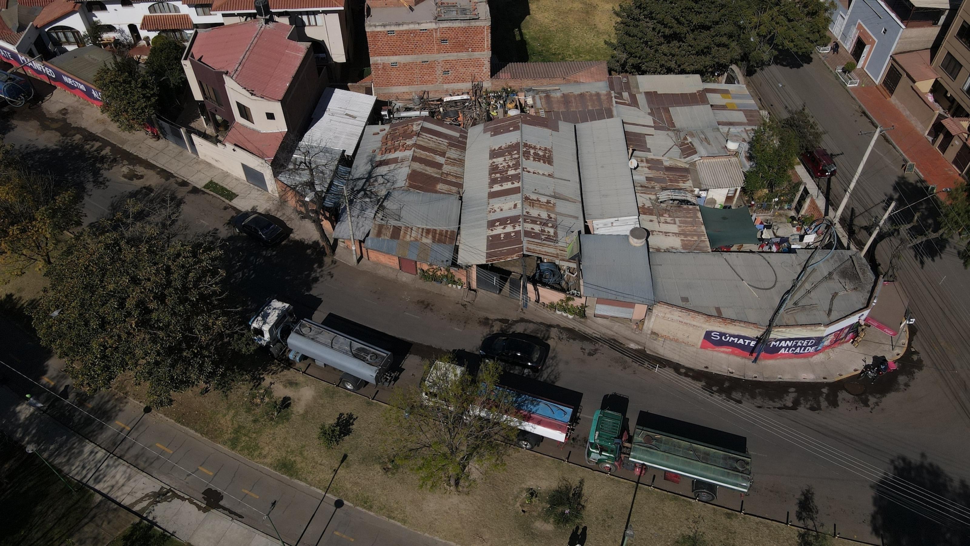 Luftaufnahme zeigt ausgetrockneten Parkstreifen, an dem hintereinander mehrer Tankwagen stehen. Parallel zu ihnen ist ein Block mit niedrigen Gebäuden oder Höfen zu sehen, die mit rostenden Blechdächern gedeckt sind.