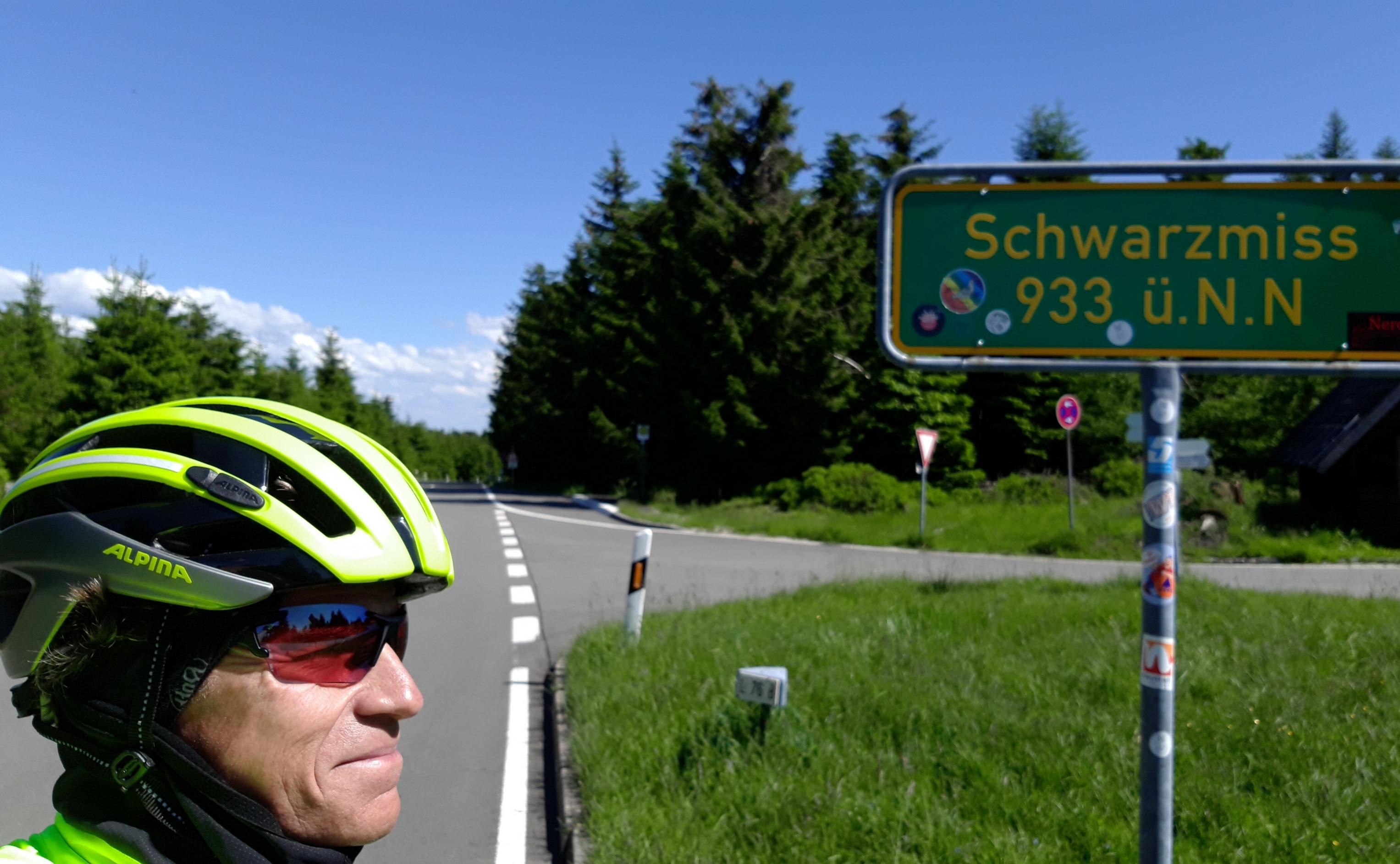 Der Autor Martin C Roos mit Radhelm posiert neben dem grünen Schild, dass die Passhöhe benennt.