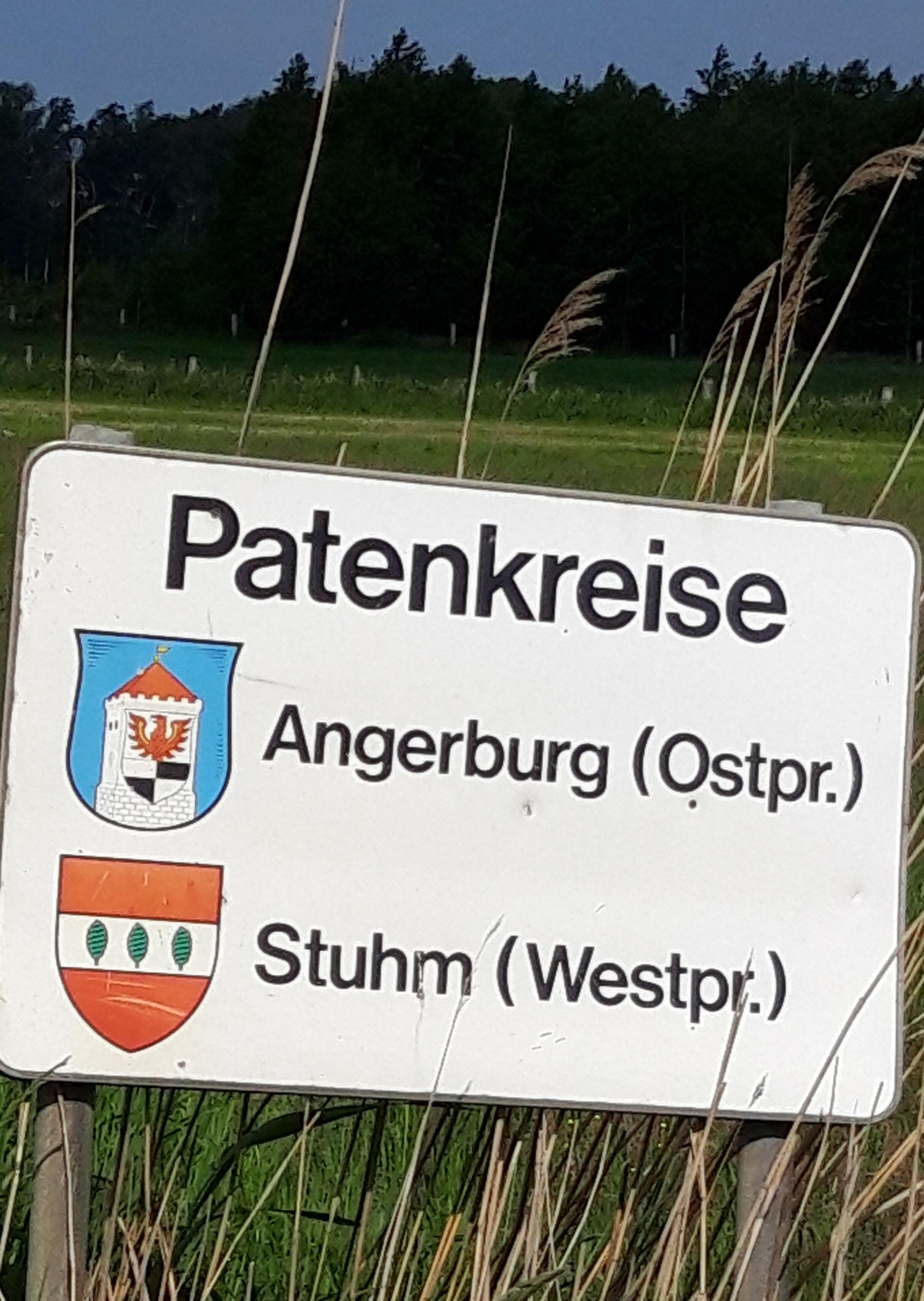Auf weißem Schild am Straßenschild ist zu lesen: „Patenkreise: Angerburg (Ostpreußen), Stuhm (Westpreußen)“, jeweils mit Wappen.