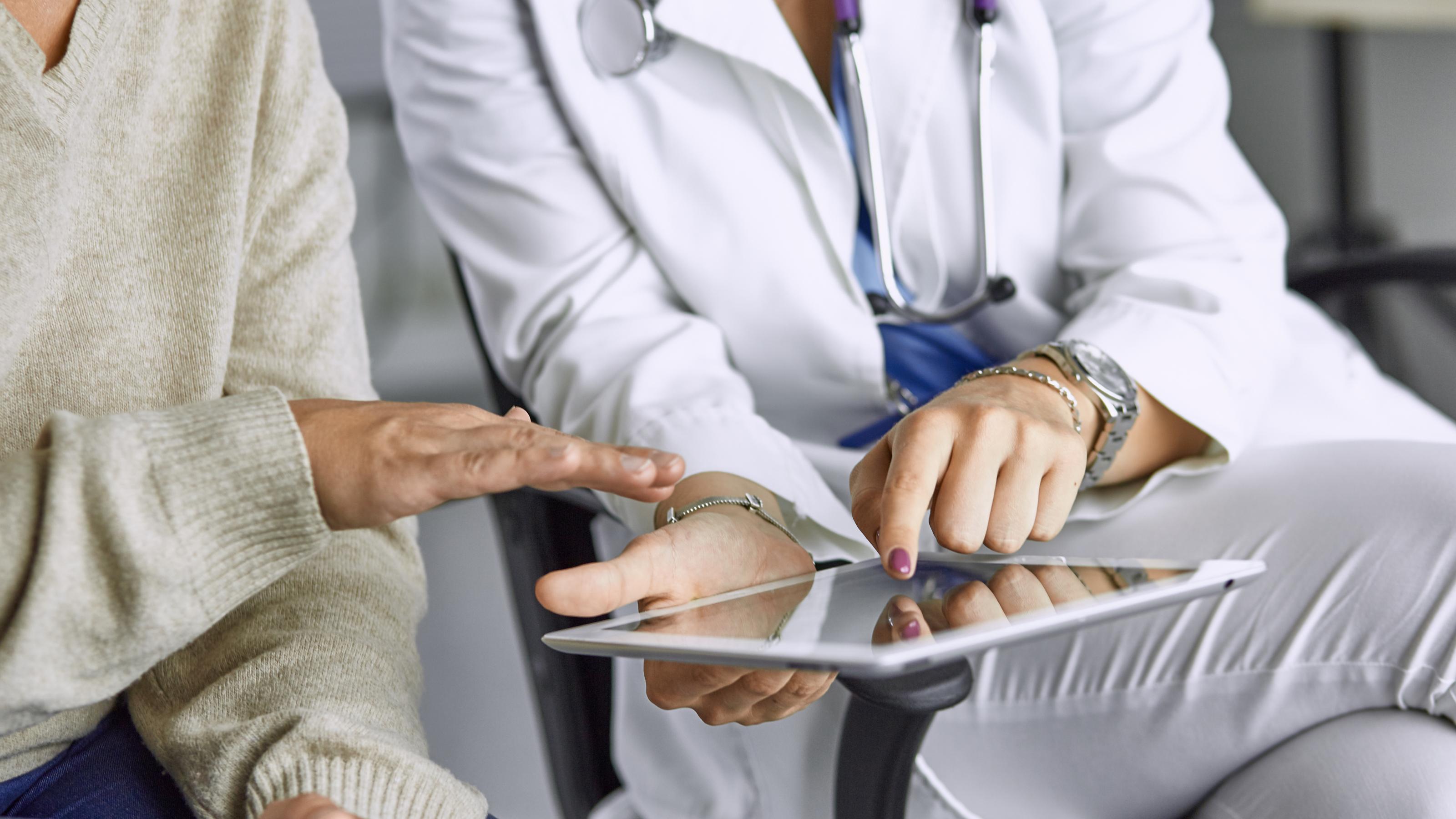 Eine junge Ärztin zeigt einer älteren Patientin medizinische Informationen auf einem Tablet.
