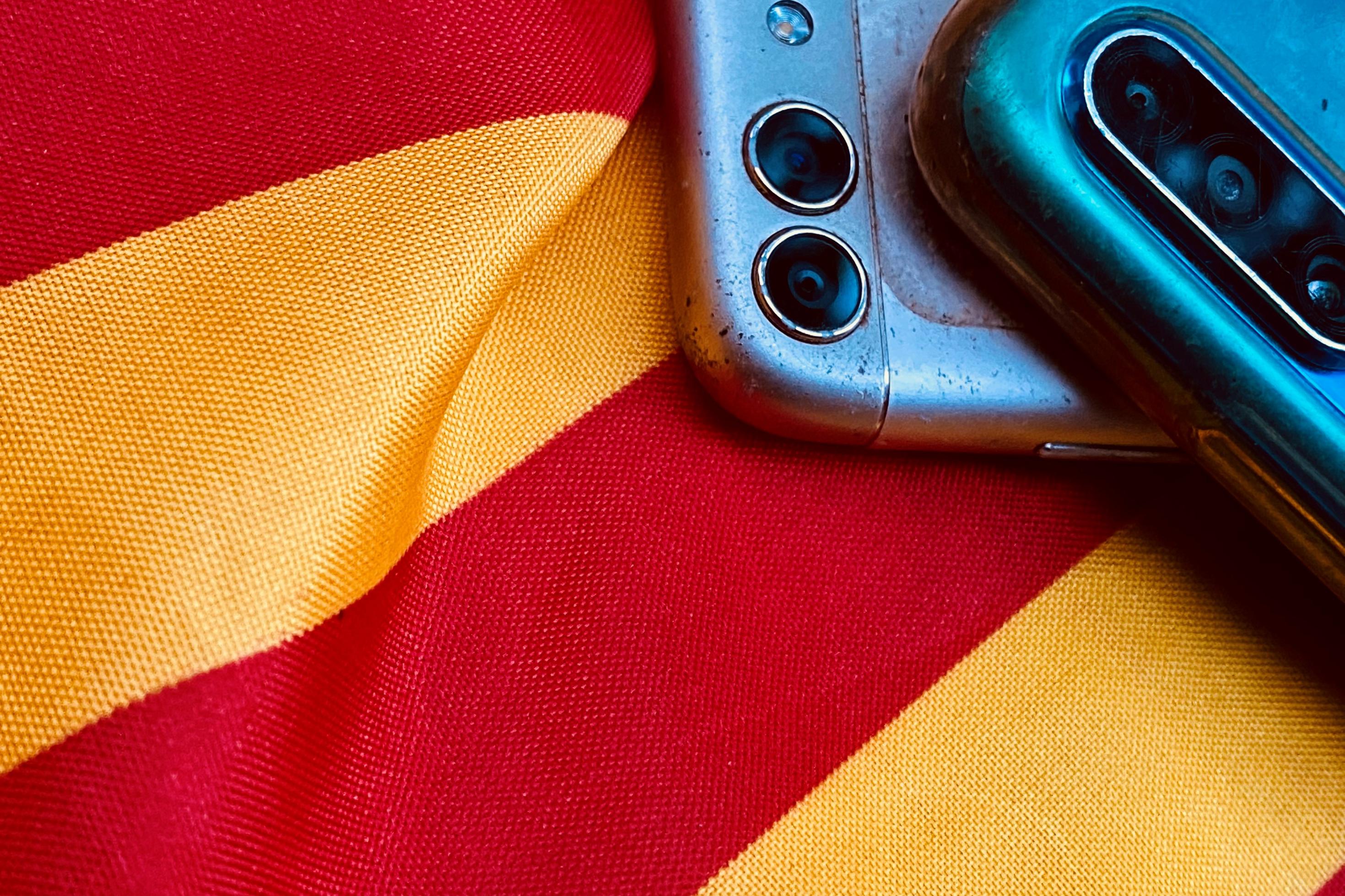 Auf einer gelbrot gestreiften katalanischen Fahne liegen zwei Smart Phones.