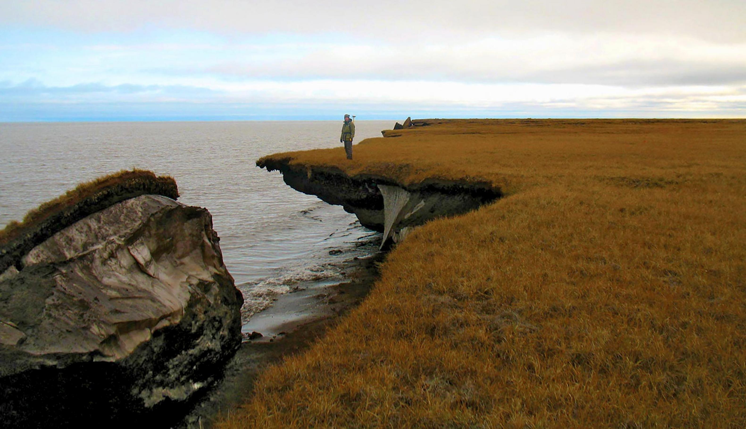Ein Mann steht an einer Küste, von der ein Stück abgebrochen ist.