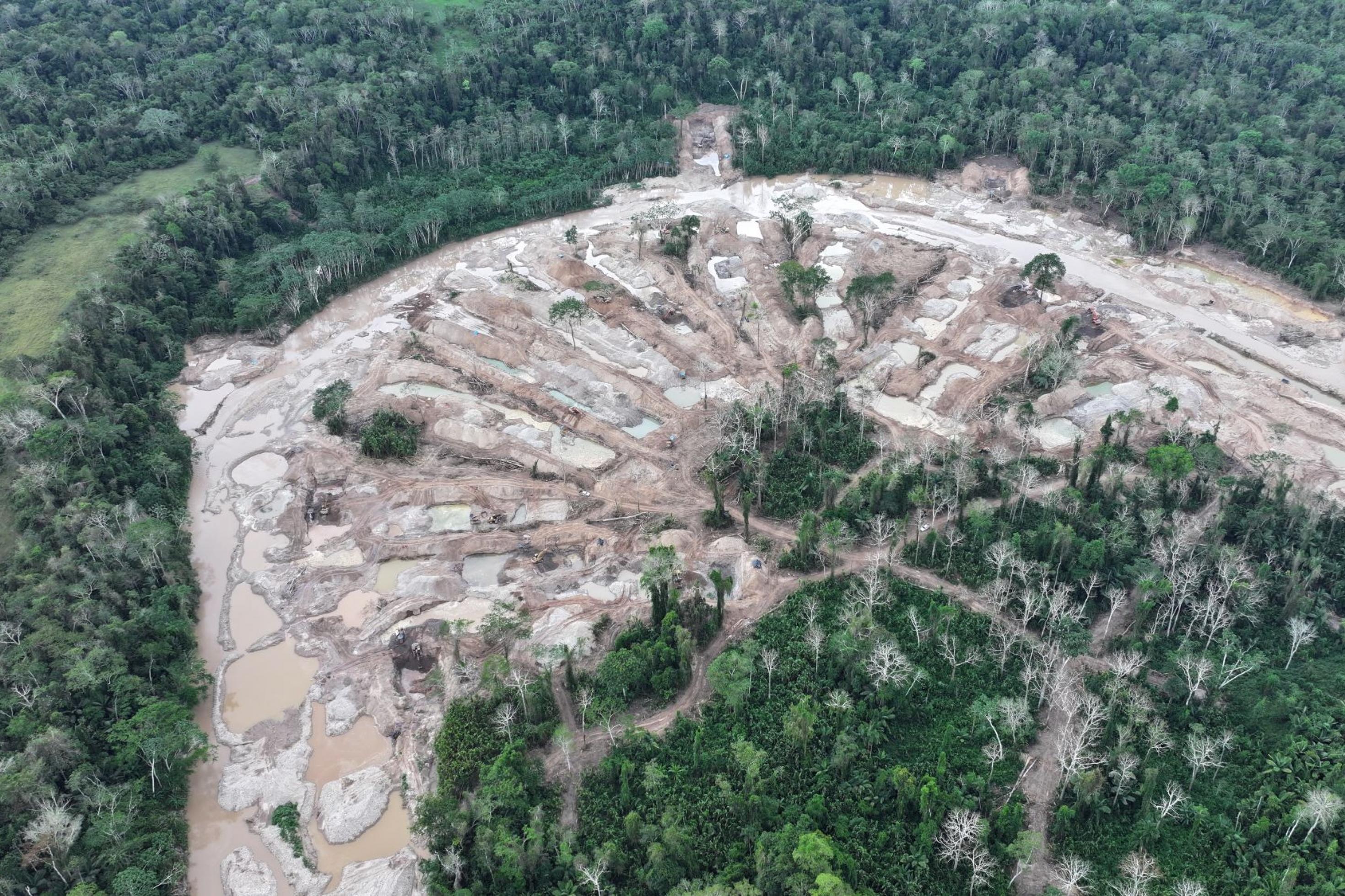 Luftbild einer Flußschlaufe im Regenwald. Das Flußufer und die angrenzenden Flächen sind abgeholzt, zeigen Sand- und Kieshaufen und Tümpel.
