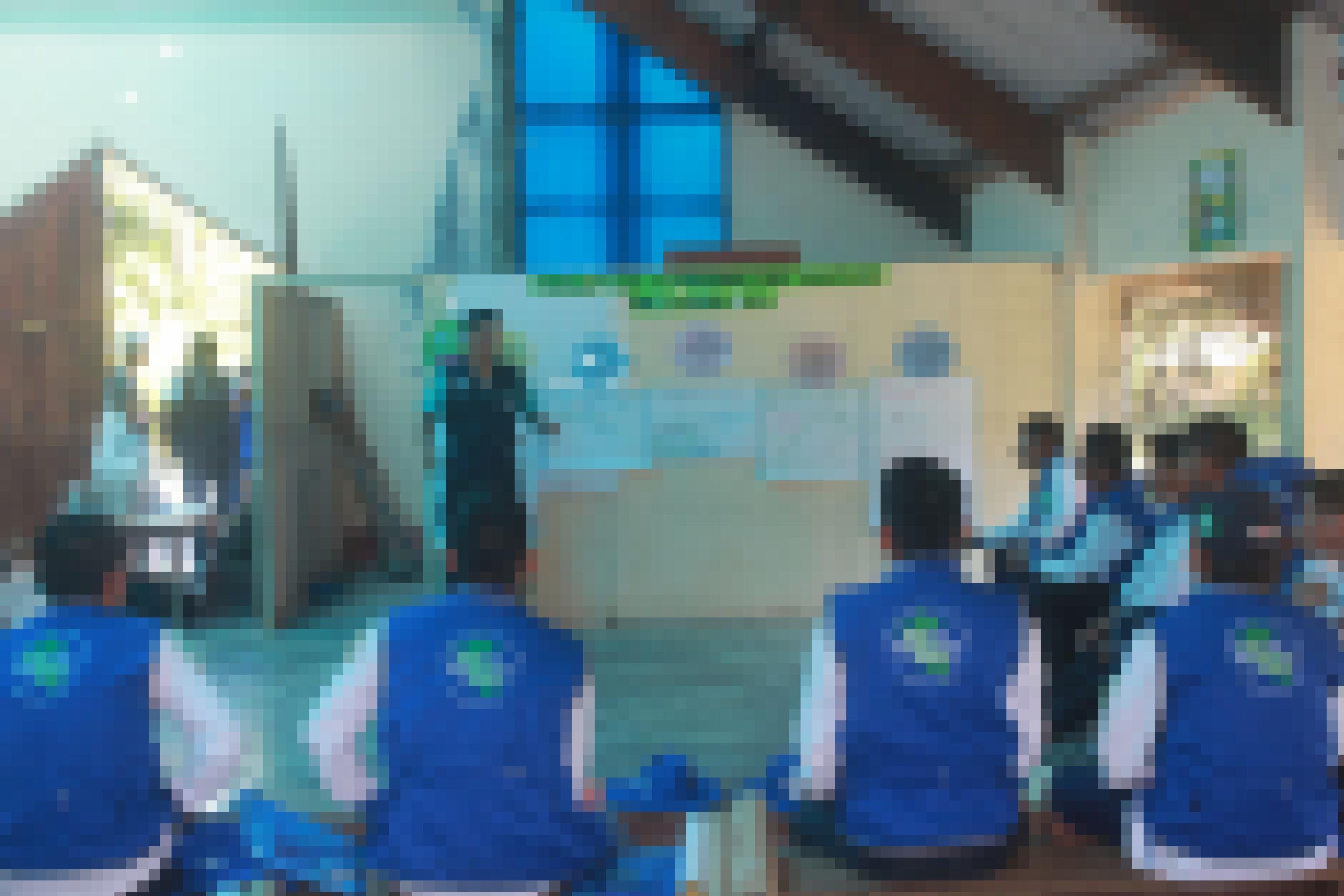 Eine Gruppe von rund 15 Männern in blauen Westen sitzen im Kreis und horchen einem jungen Mann zu, der an einem Wandbild erklärt, wie man Malariaprophylaxe betreibt.