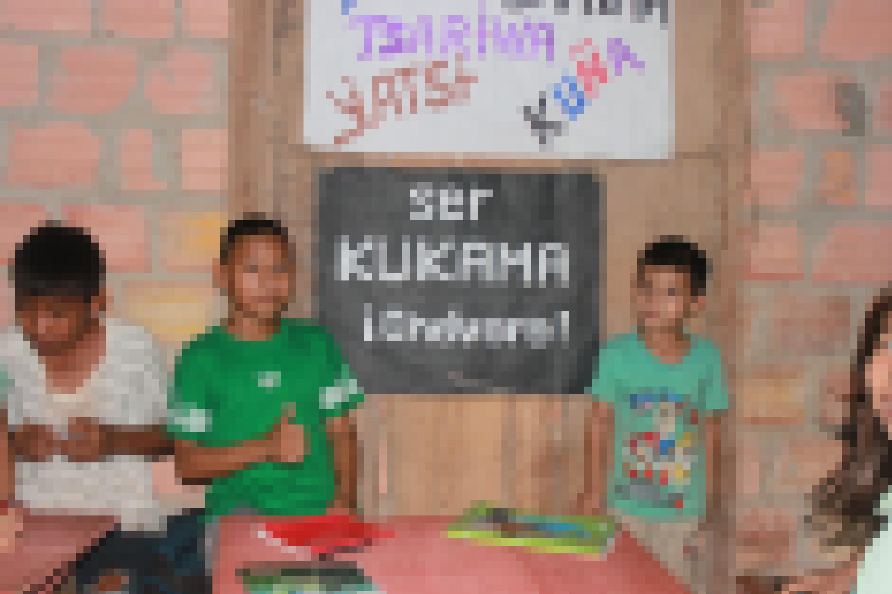 Holzwand mit schwarzem Papier, darauf in weissen Lettern: Ser kukama, chevere! Kukama sein ist cool. Daneben zwei Jugendliche.