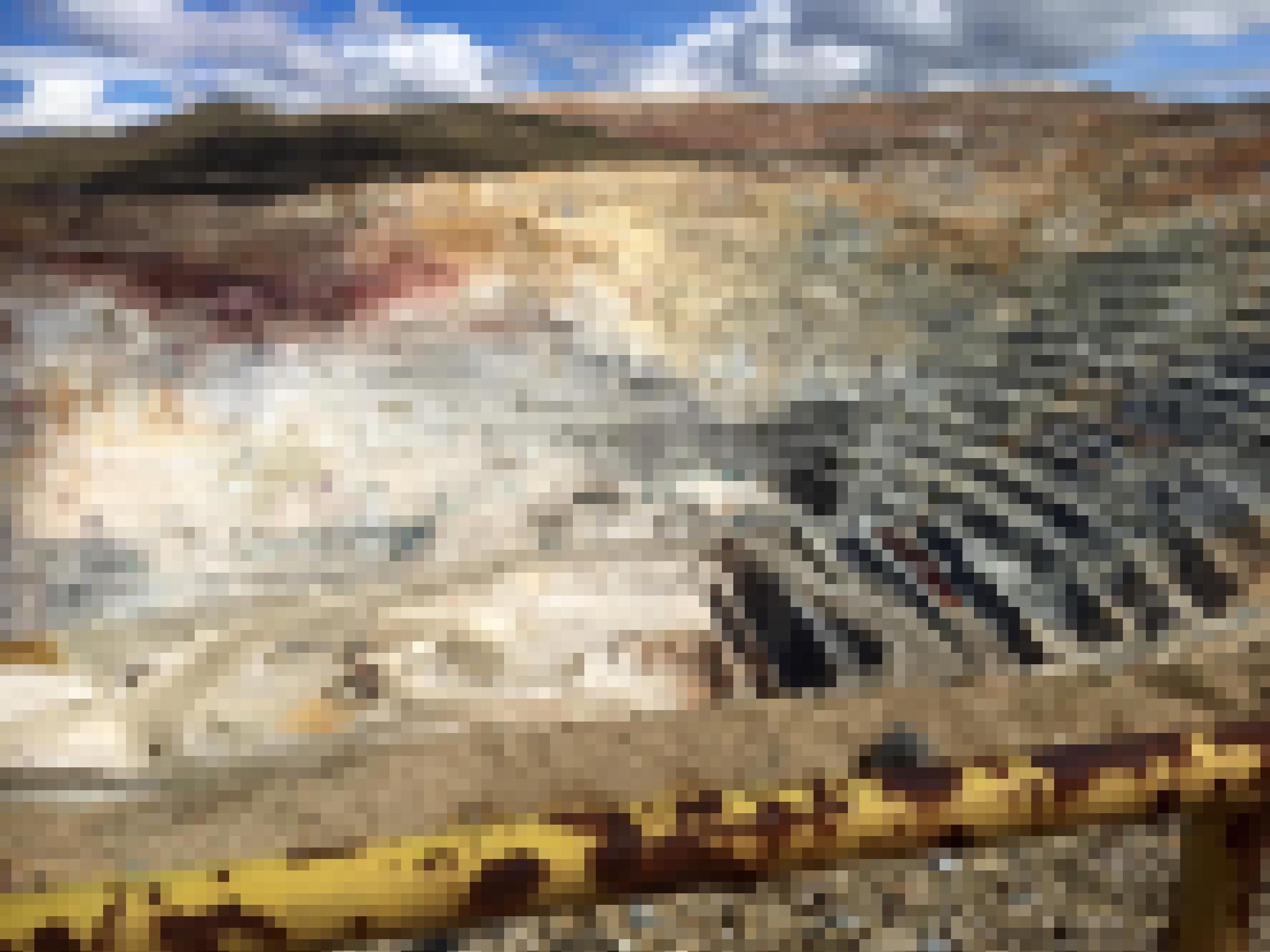 Berglandschaft, davor ein tiefer, in Rundgängen abgebauter  Krater.  Am Boden des Kraters  ist aus der Ferne eine Maschine zu sehen.