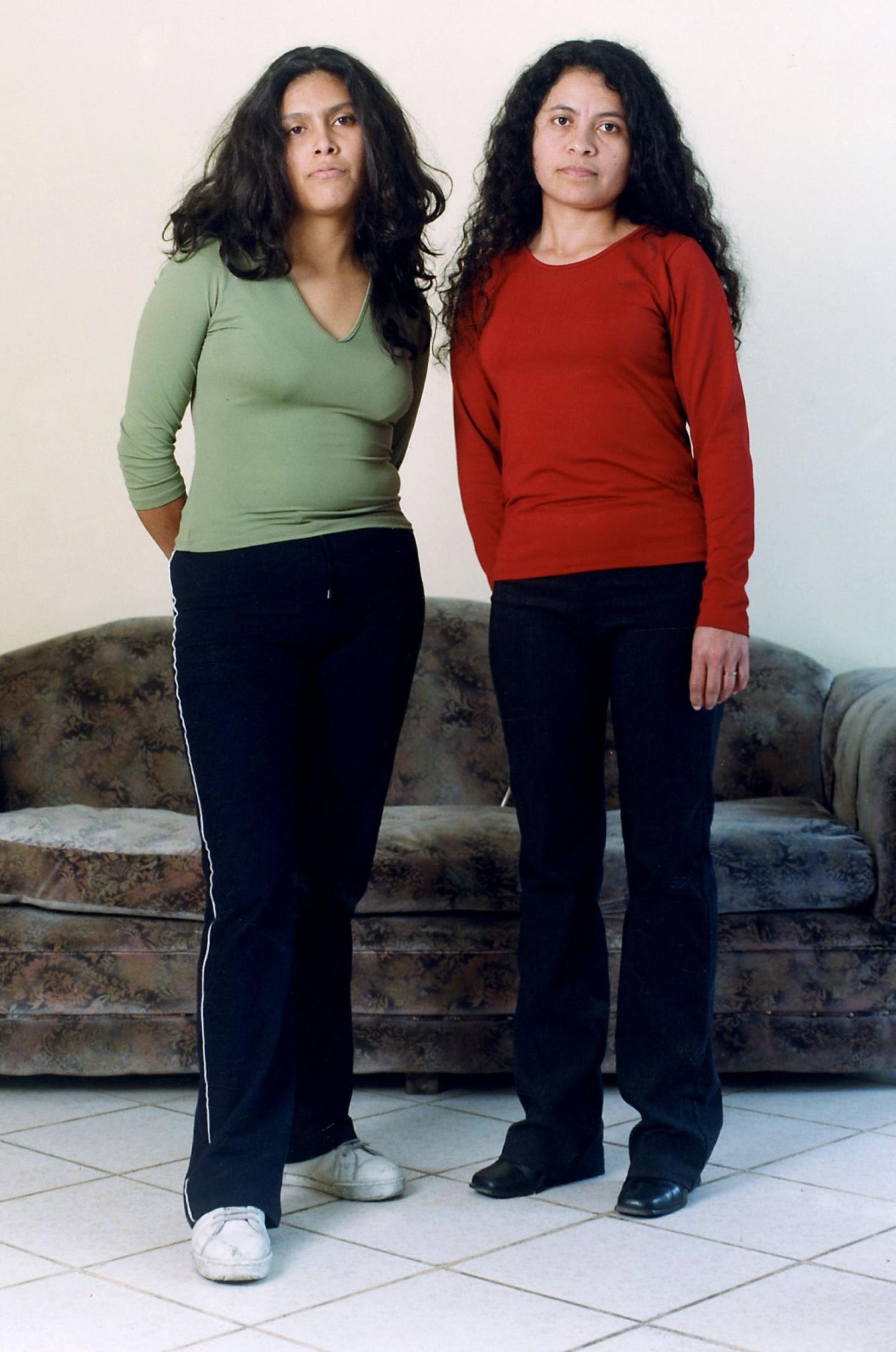 Zwei junge Frauen stehen nebeneinander und blicken in die Kamera. Beide sind ungefaehr gleich gross, haben dieselbe Hautfarbe und  tragen die langen schwarzen Haare offen.