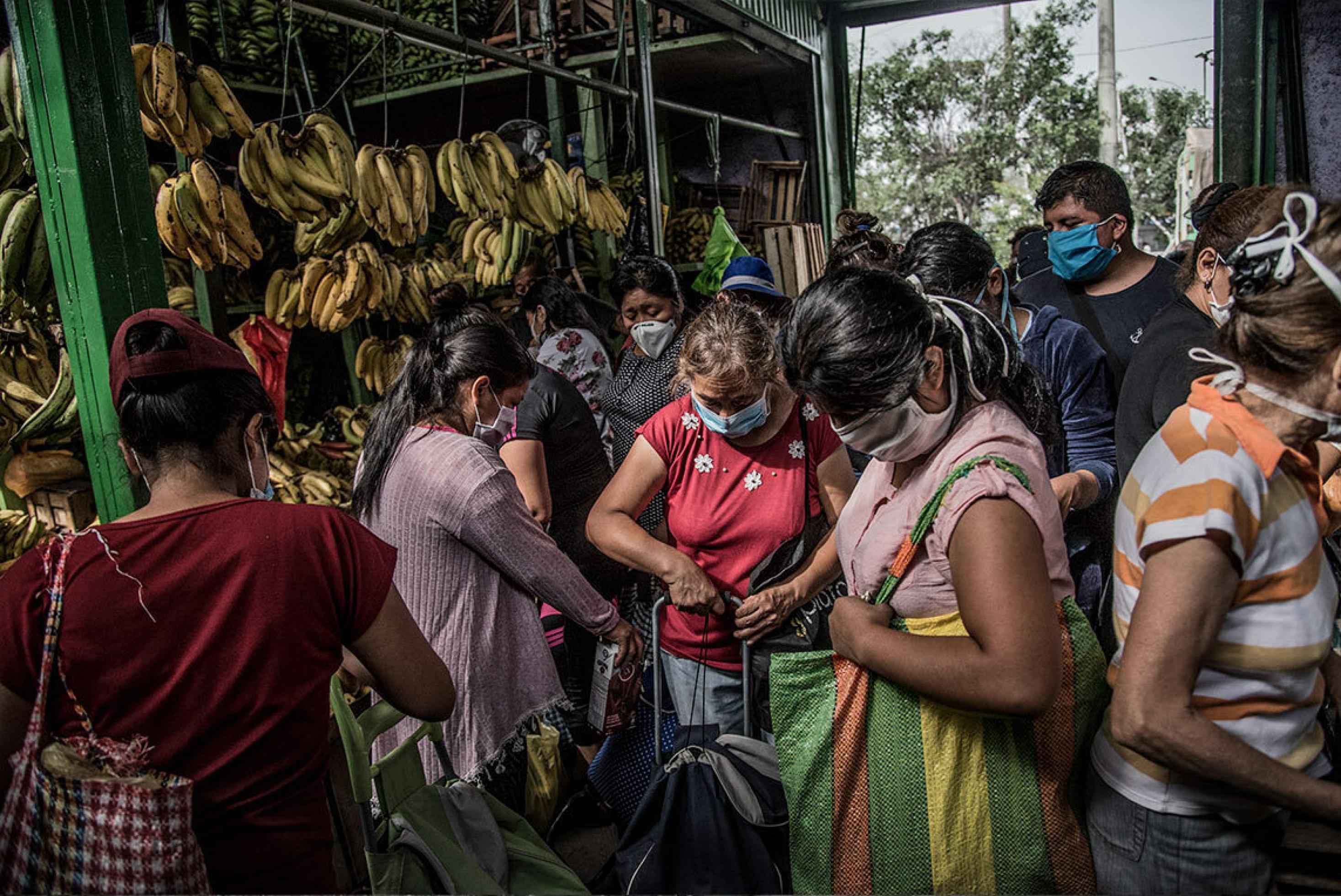 Peruanische Frauen stehen dicht gedrängt mit Tragetaschen und Wägelchen vor einem Bananenstand in einer Markthalle in Lima.