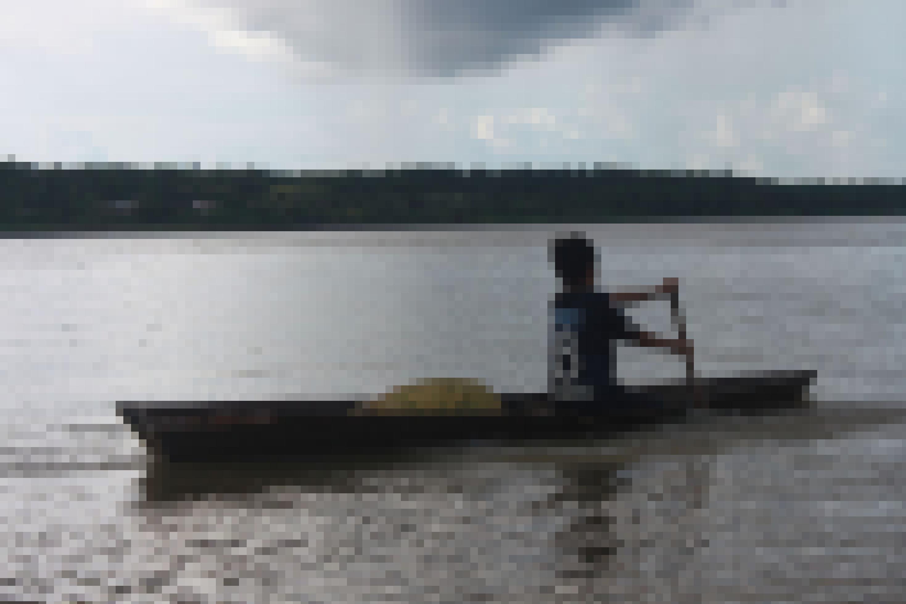 Abenddämmerung über einem Fluss. Ein Holzkanu, man sieht den Rücken eines Jungen, der im Kanu sitzt und paddelt.