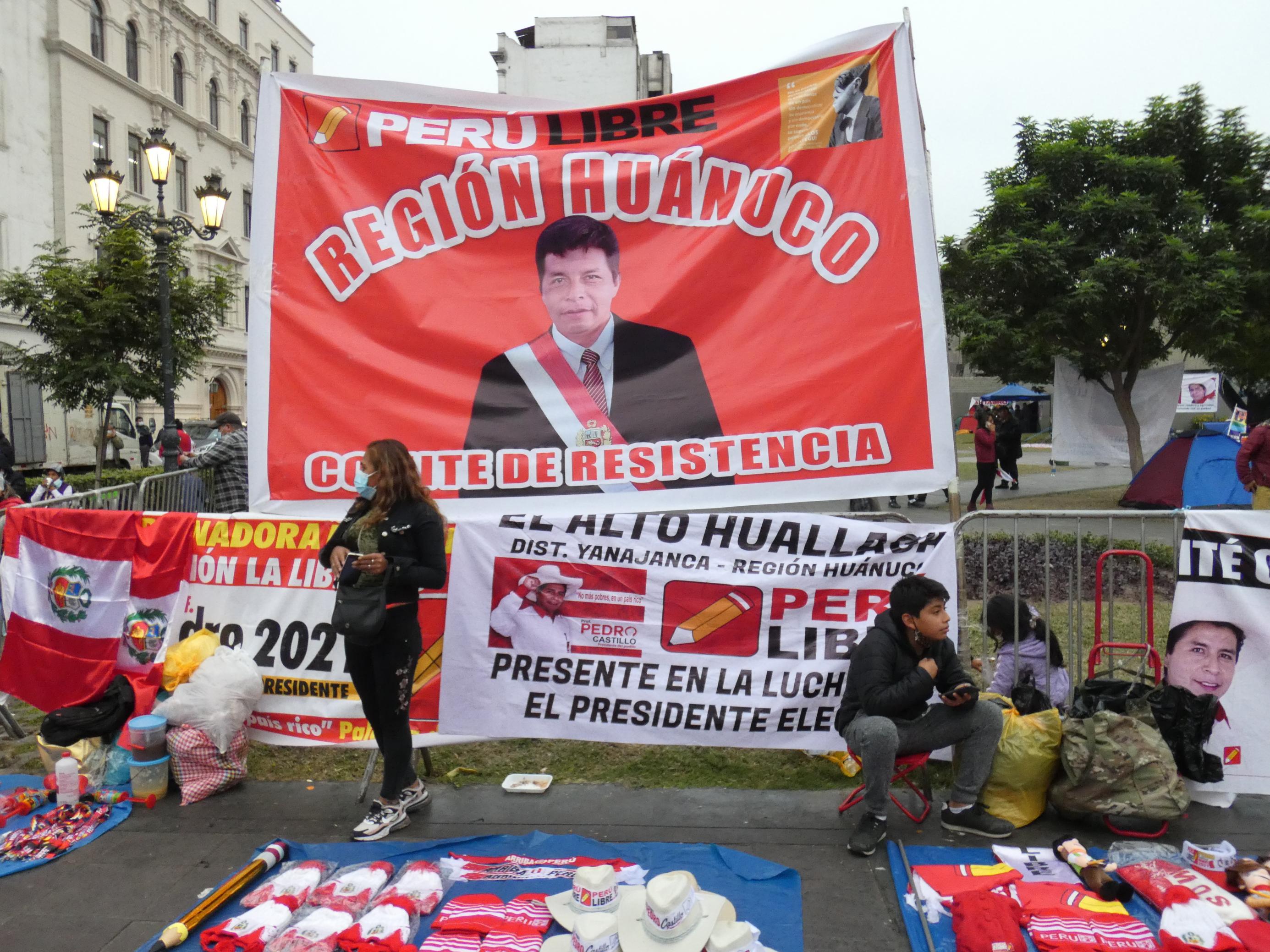 Große rote Banderole, darauf ein Mann mit einer Präsidentenschärpe. Auf dem Boden davor werden Devotionalien verkauft.