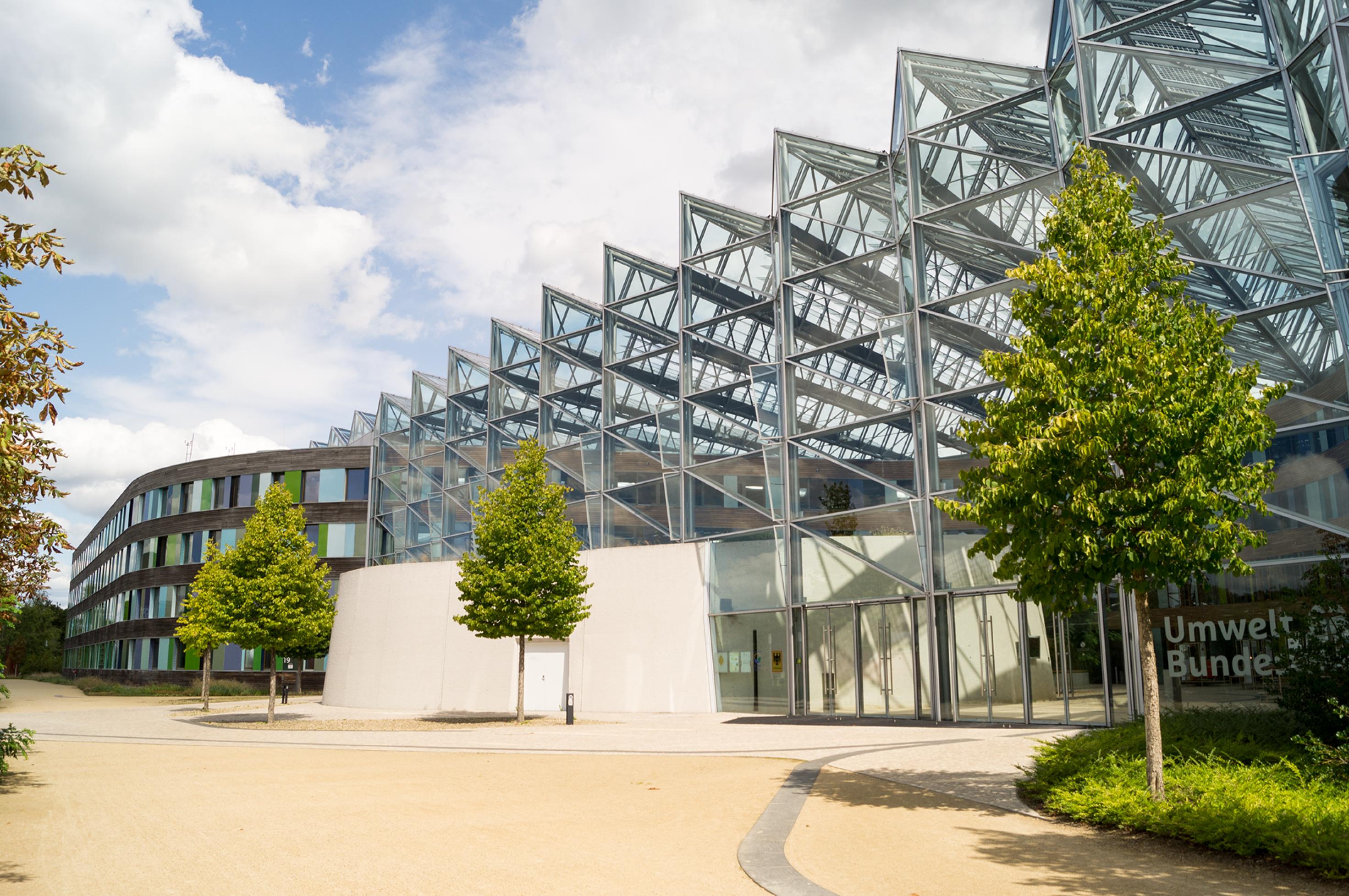 Modernes Gebäude mit einem treibhausartigen Eingangsbereich und geschwungener Holzfassade.