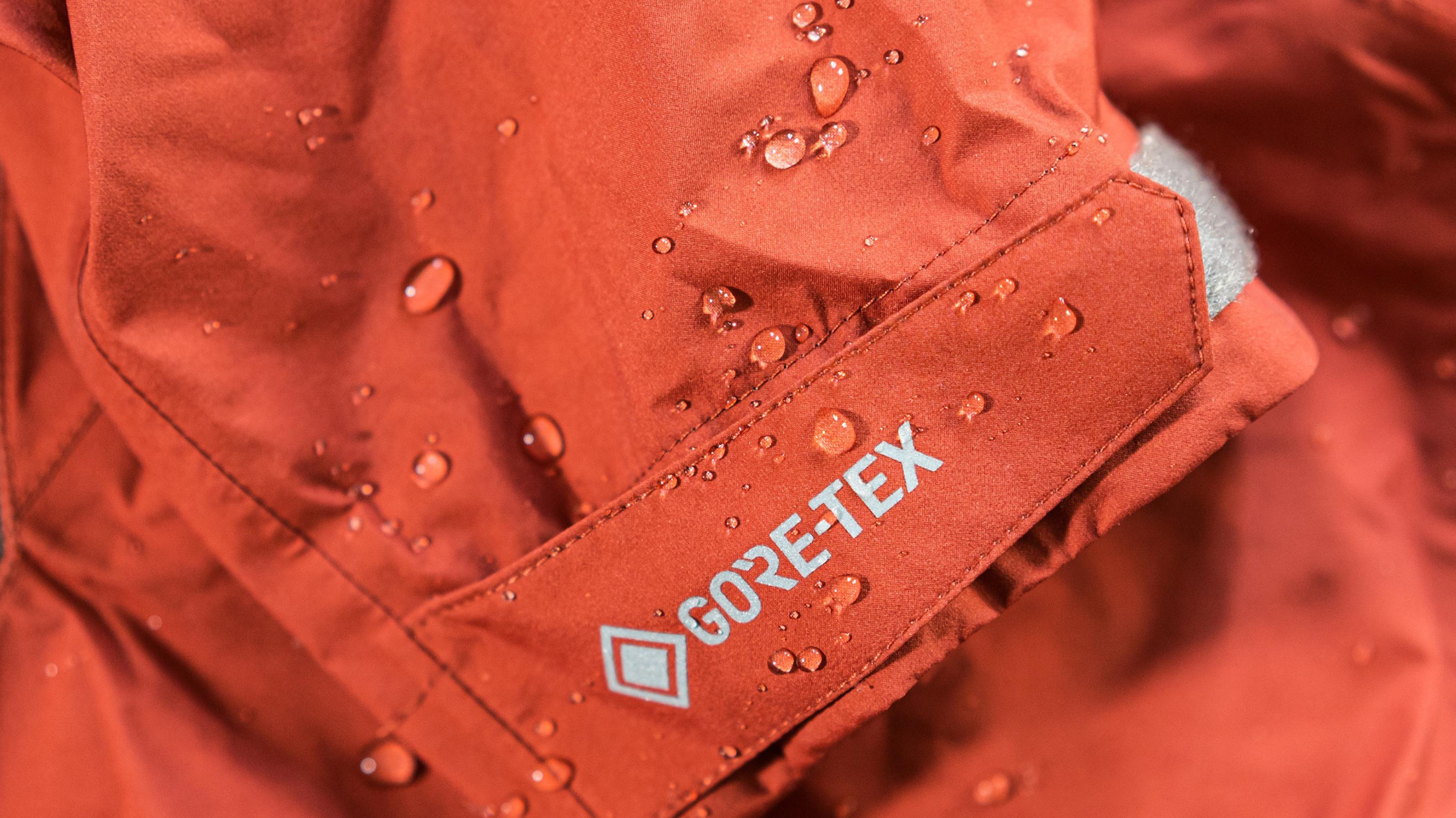 Ausschnitt einer orange-roten Outdoor-Jacke mit abperlenden Wassertropfen