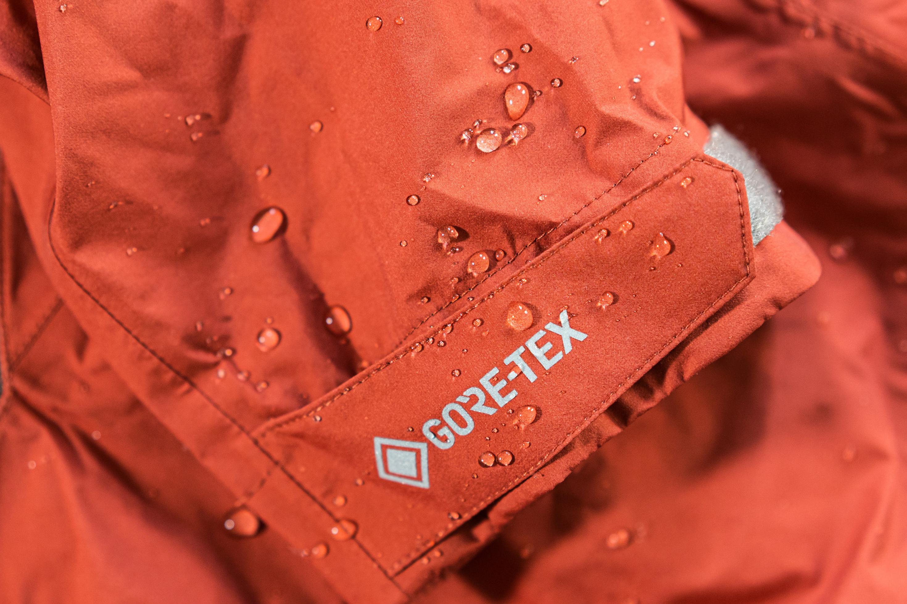 Ausschnitt einer orange-roten Outdoor-Jacke mit abperlenden Wassertropfen