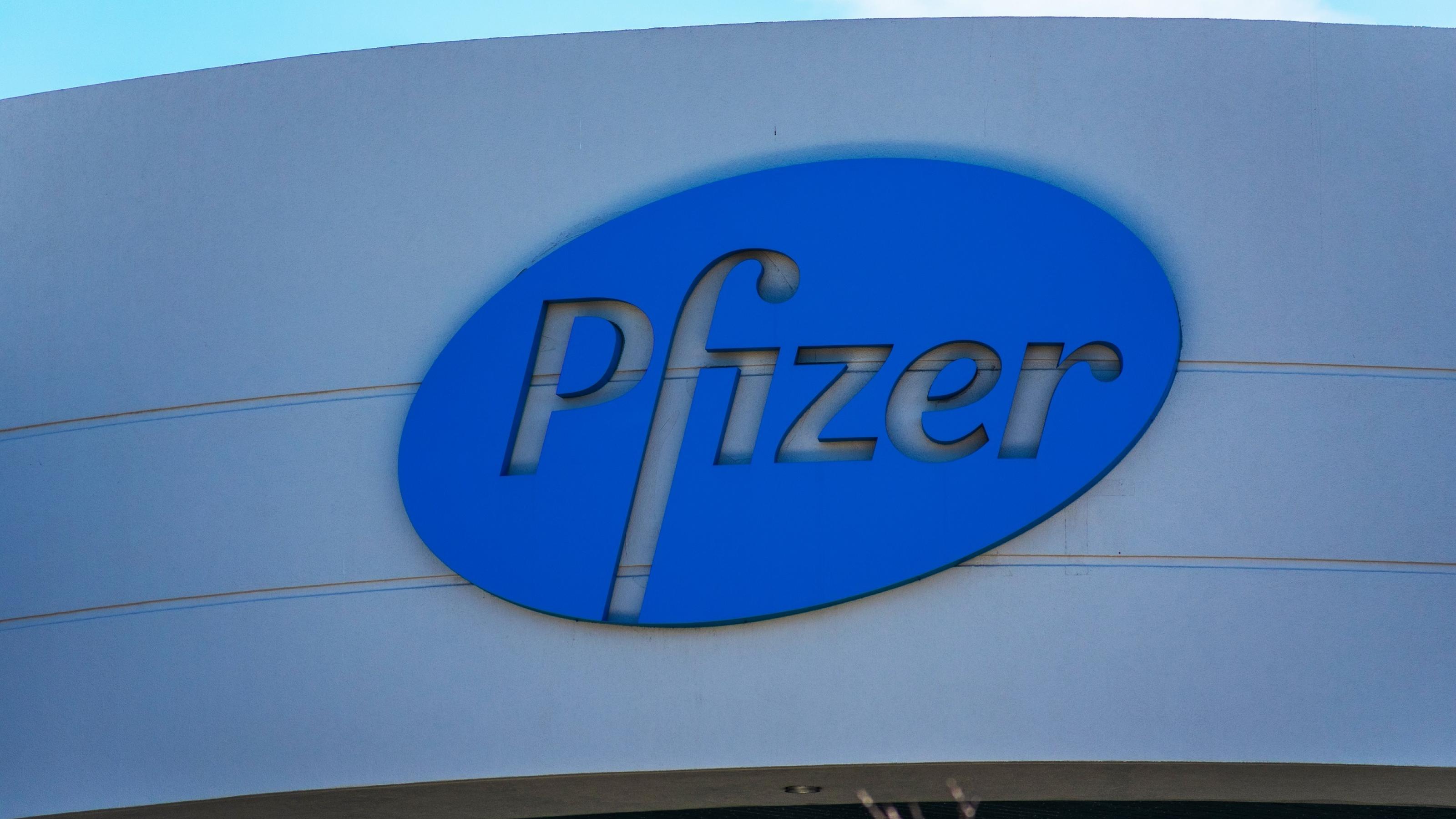 Logo mit dem Schriftzug Pfizer auf blauem Grund an der hellgrauen Fassade eines modernen Gebäudes