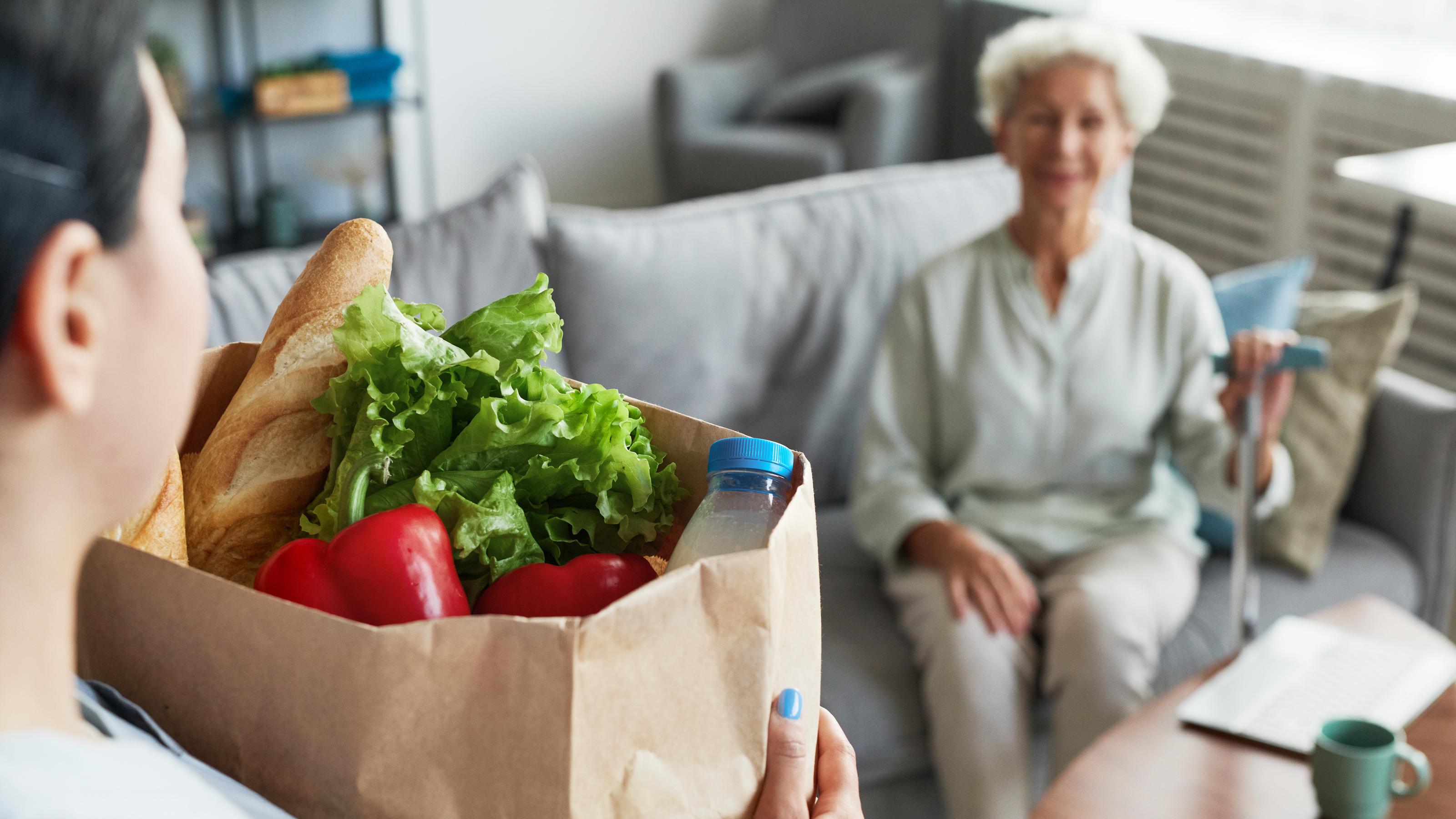 Eine Frau bringt einer alten Dame eine Tüte voll frischer Lebensmittel. Für solche Hilfeleistungen zahlt die Pflegeversicherung nur, wenn die Anbieter zertifiziert sind.