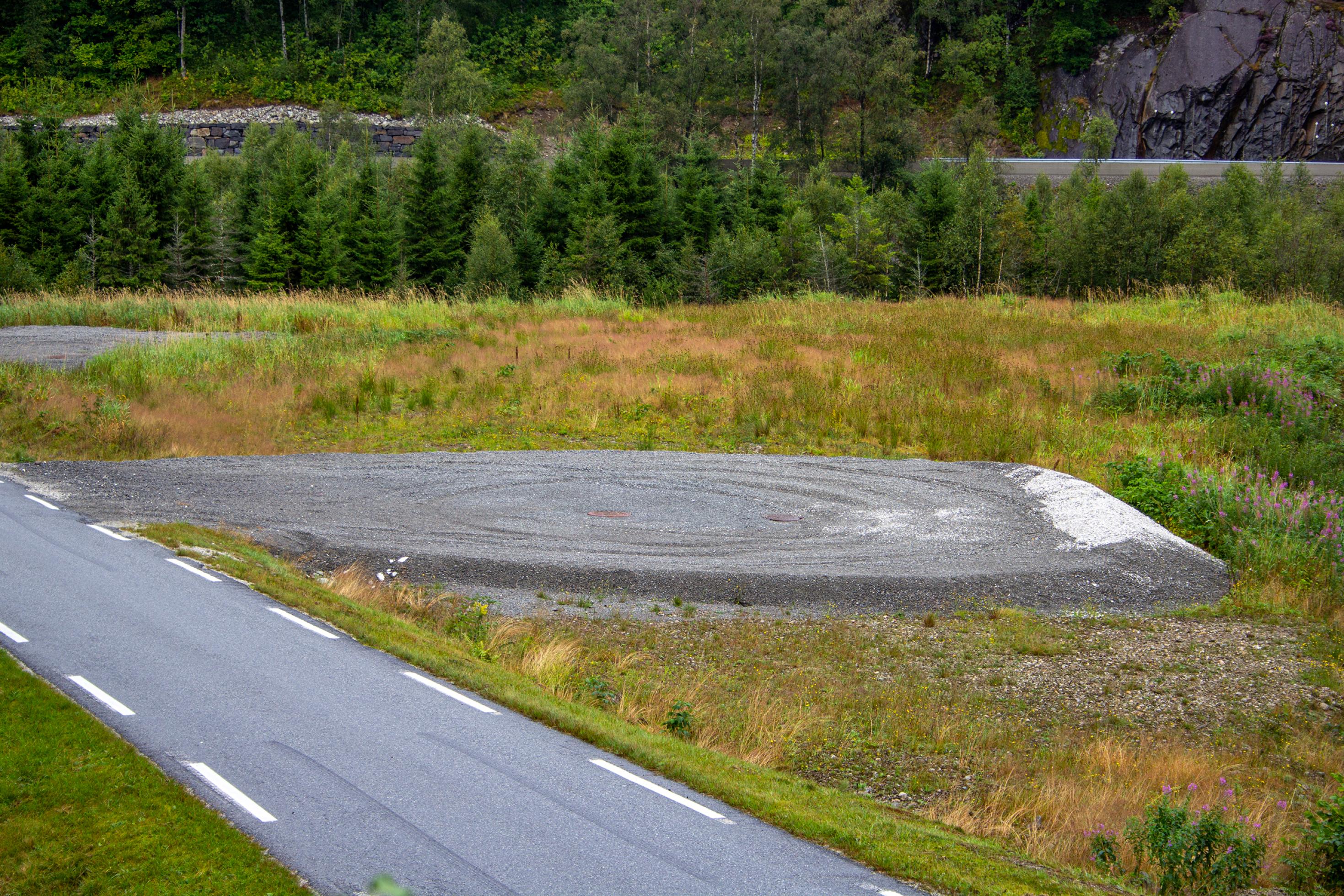 Eine Schotterfläche am Rand einer schmalen Straßen in einer bewaldeten, bergigen Landschaft