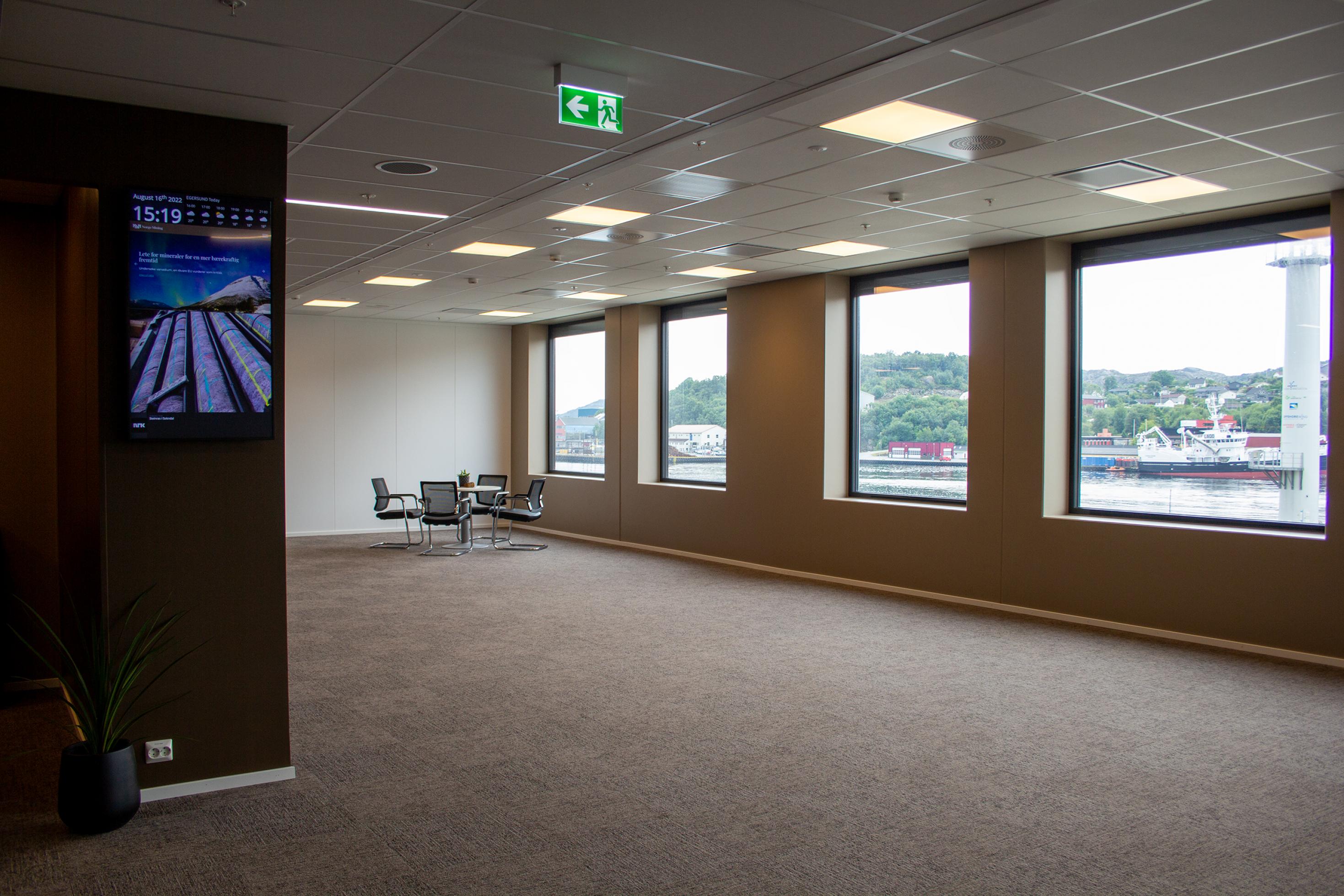 Eine große leere Büroetage mit großen Fenstern und Blick auf den Hafen; in der fernen Ecke eine Sitzgruppetbd
