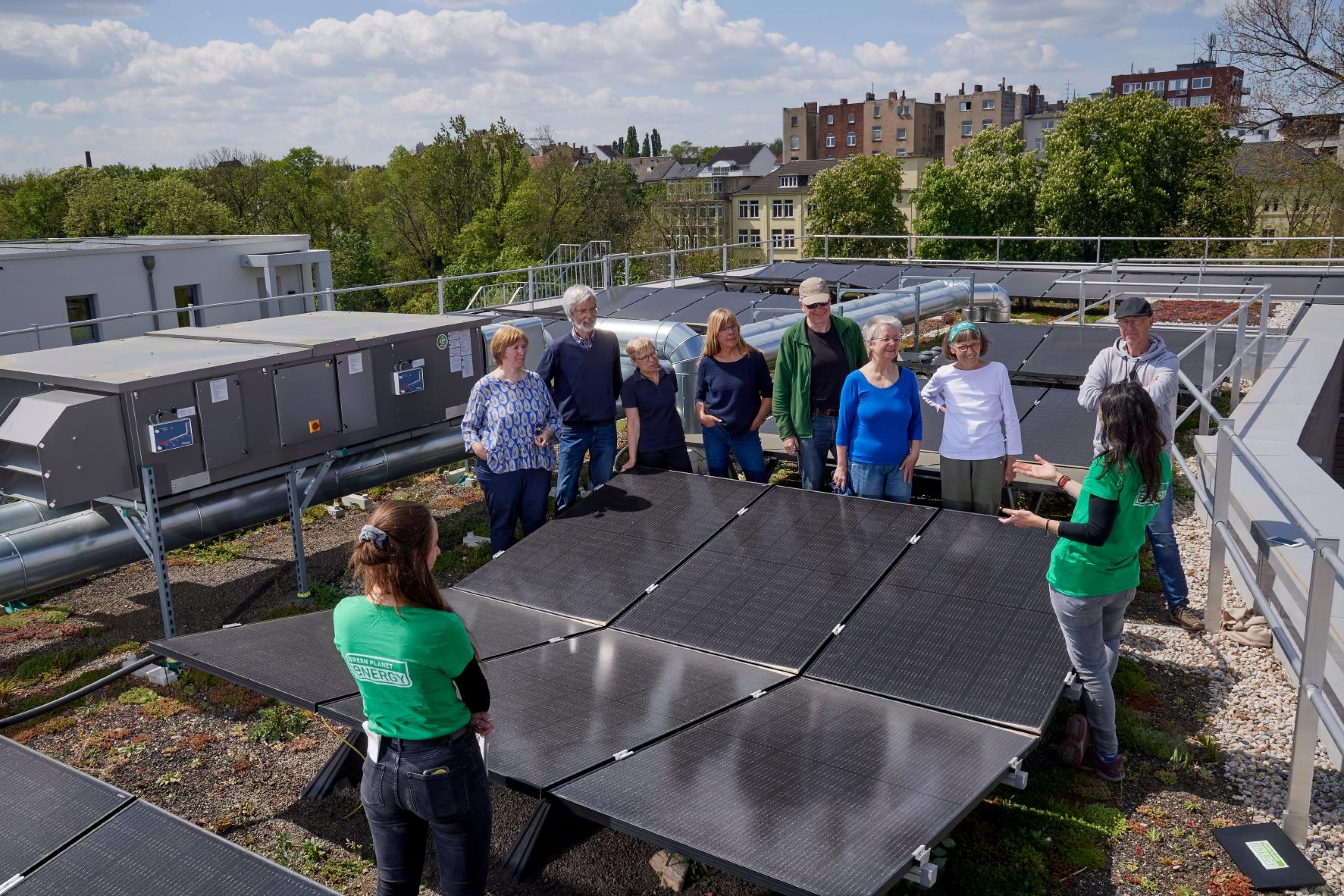 Ein knappes Dutzend Menschen, versammelt um sechs Photovoltaik-Module, auf dem Flachdach eines Mehrparteienhauses