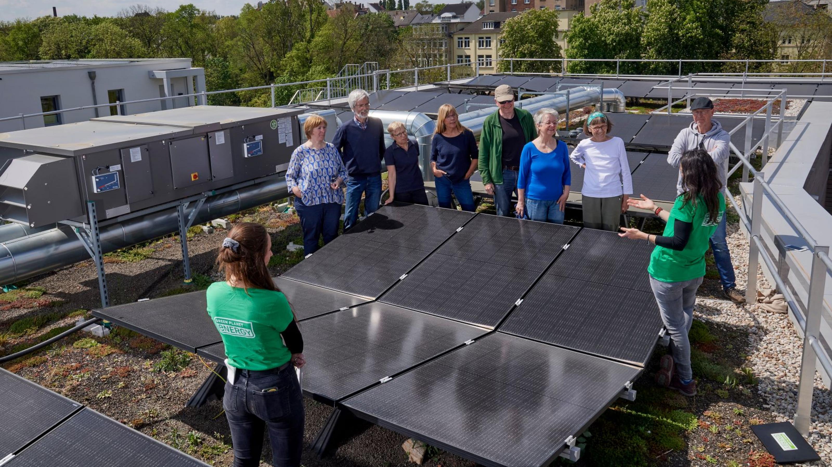 Ein knappes Dutzend Menschen, versammelt um sechs Photovoltaik-Module, auf dem Flachdach eines Mehrparteienhauses