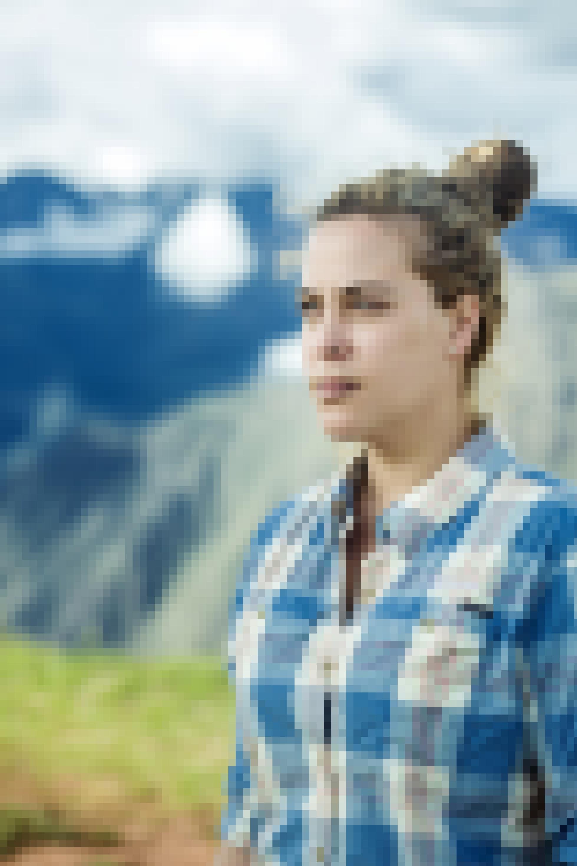 Junge Frau mit losem Dutt in Holzfellerhemd vor unscharfer Berglandschaft.
